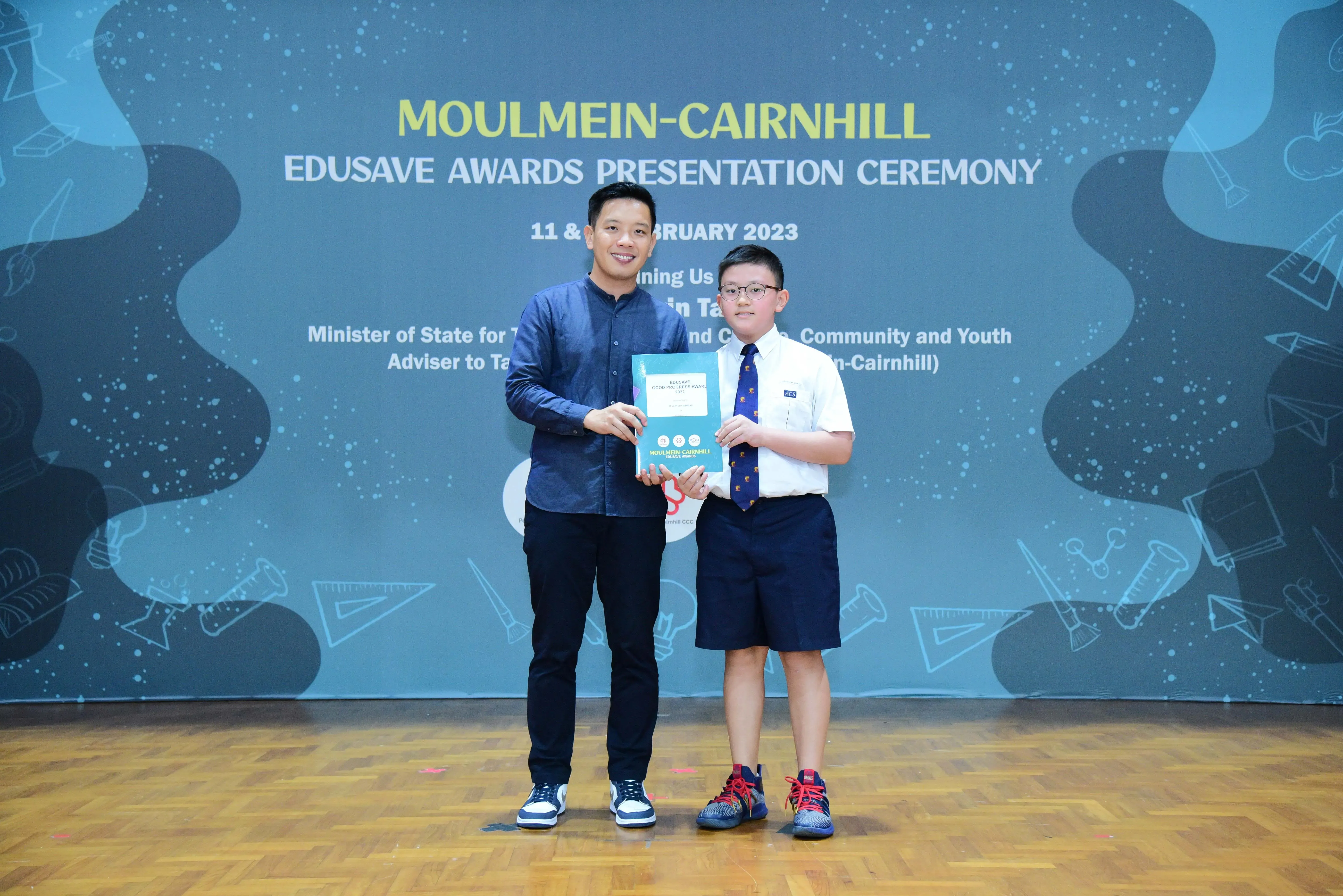 An adult and a uniformed student hold a certificate together at the Moulmein-Cairnhill Edusave Awards Ceremony 2023.