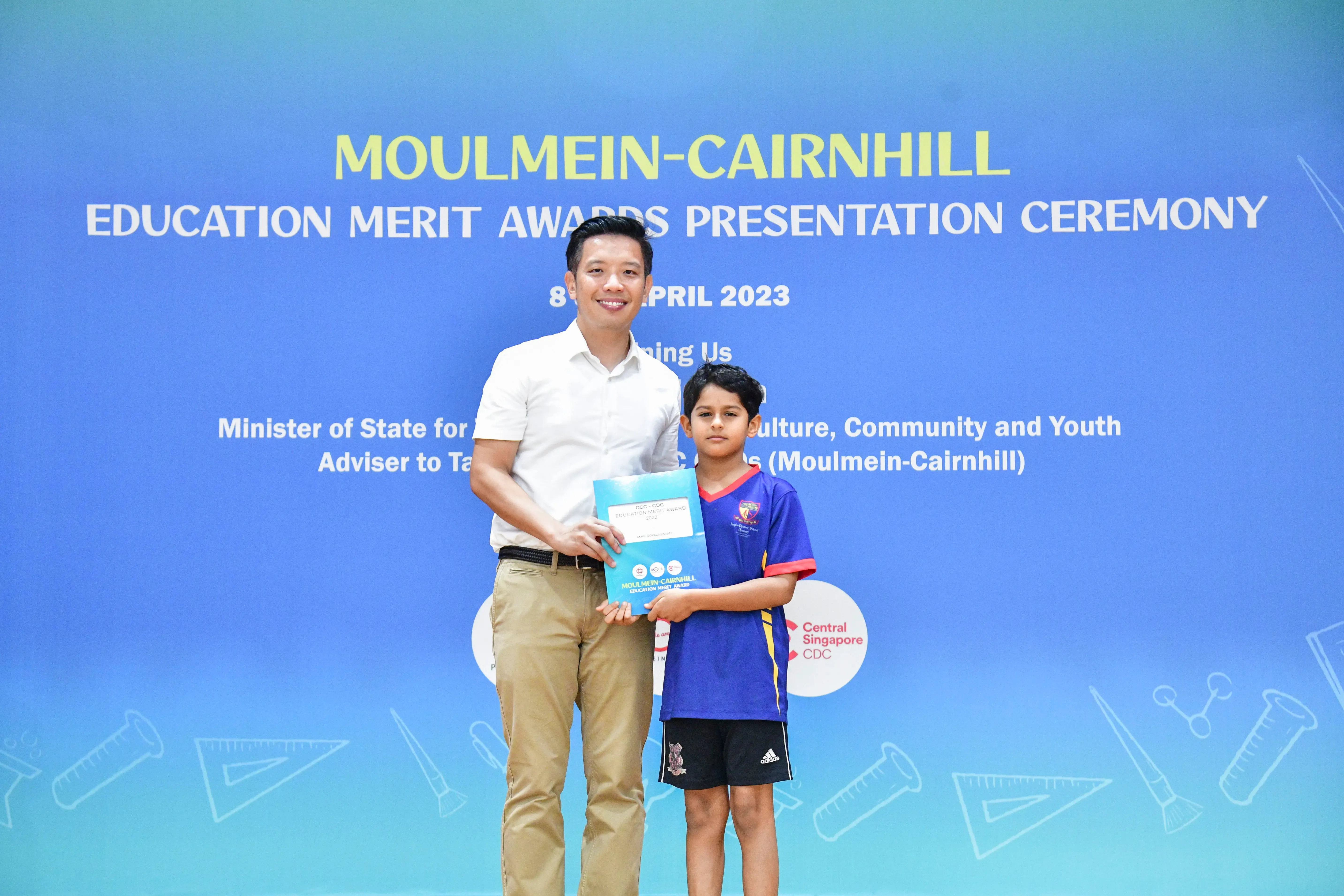 A man and a young boy hold an award certificate at the Moulmein-Cairnhill Education Merit Awards Ceremony, April 2023.
