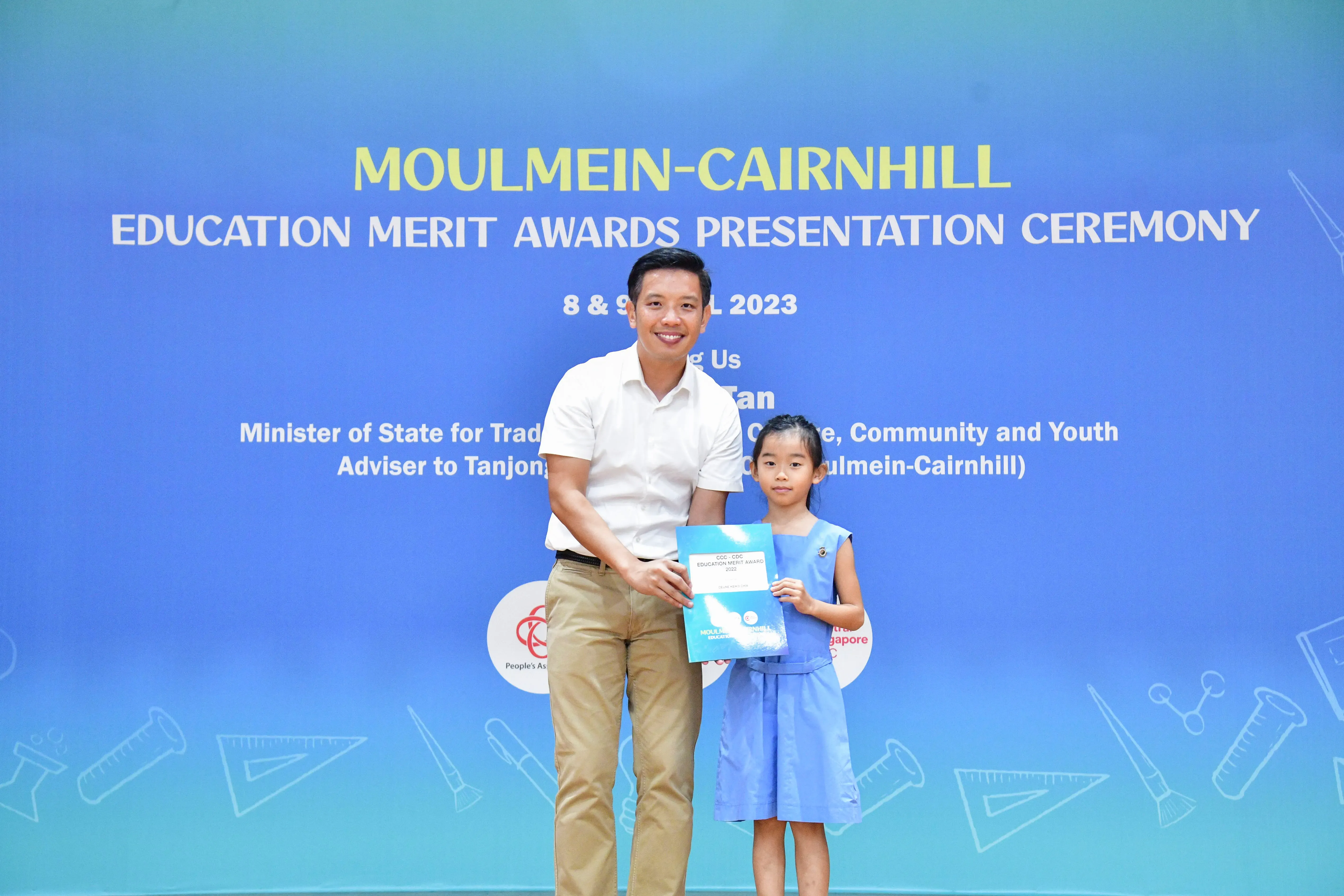 A man and a young girl hold a certificate together at the Moulmein-Cairnhill Education Merit Awards Ceremony 2023.