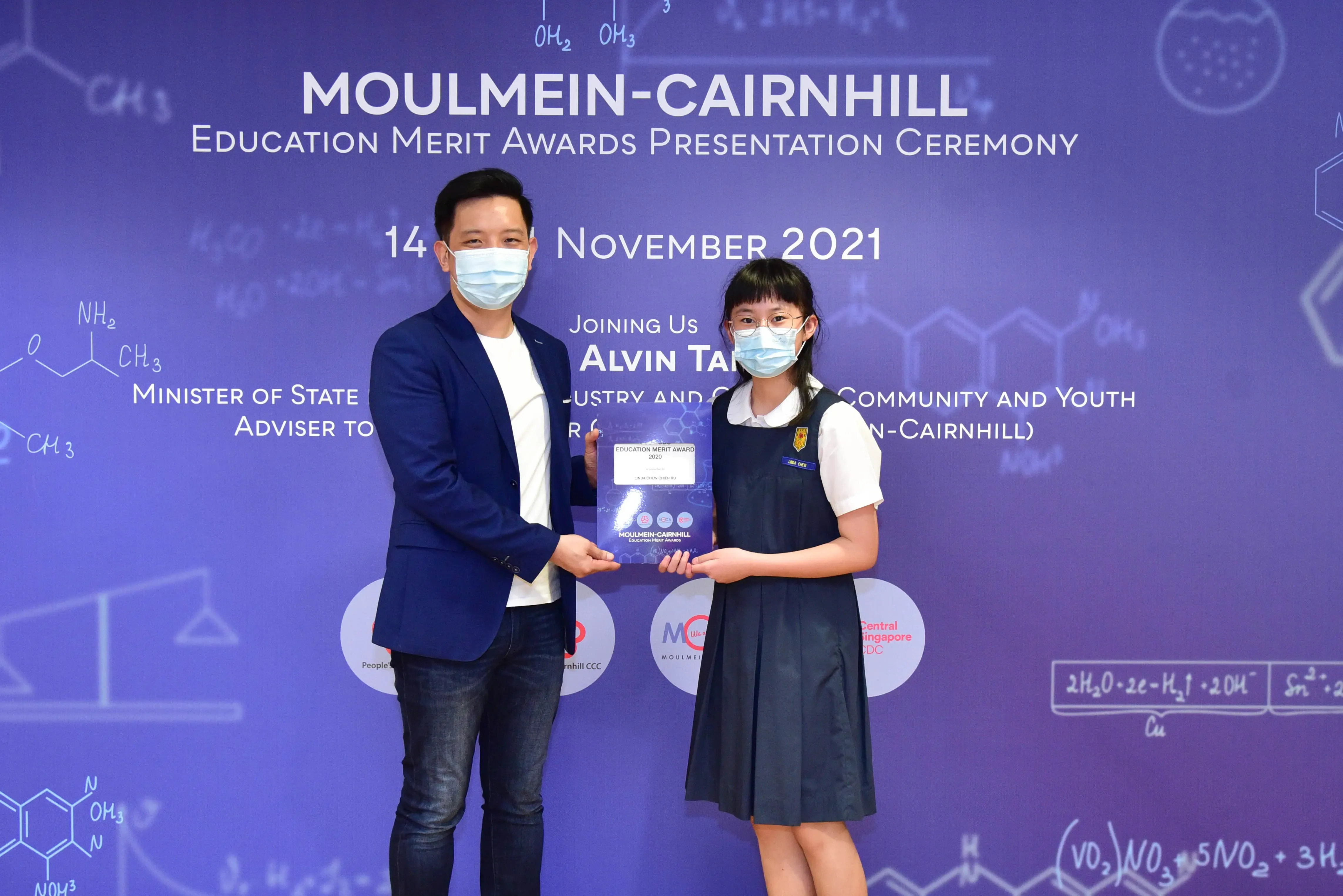 Two masked individuals hold an award certificate at the Moulmein-Cairnhill Education Merit Awards Ceremony, November 2021.