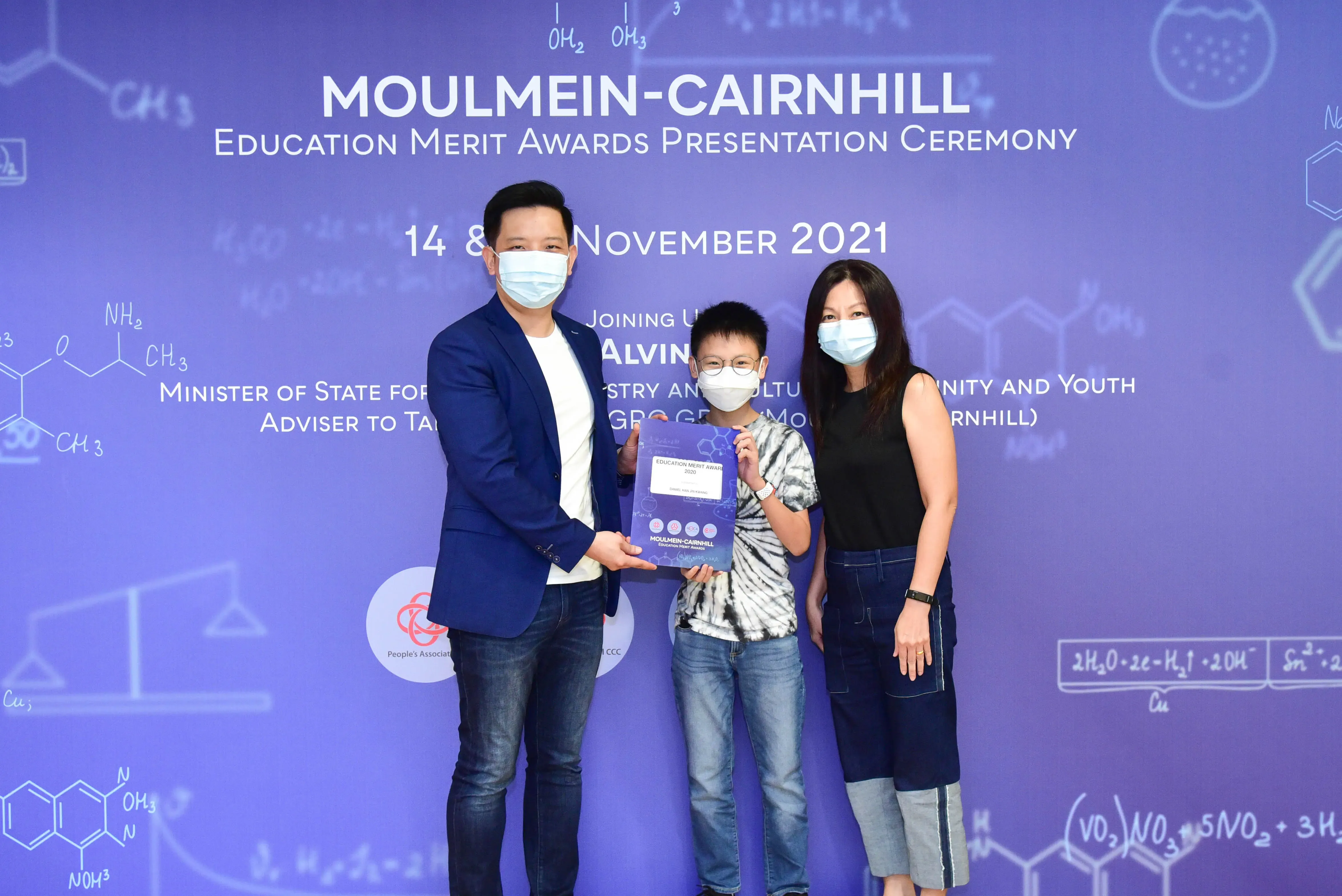 Three masked people pose at the Moulmein-Cairnhill Education Merit Awards Ceremony, November 2021, holding an award.