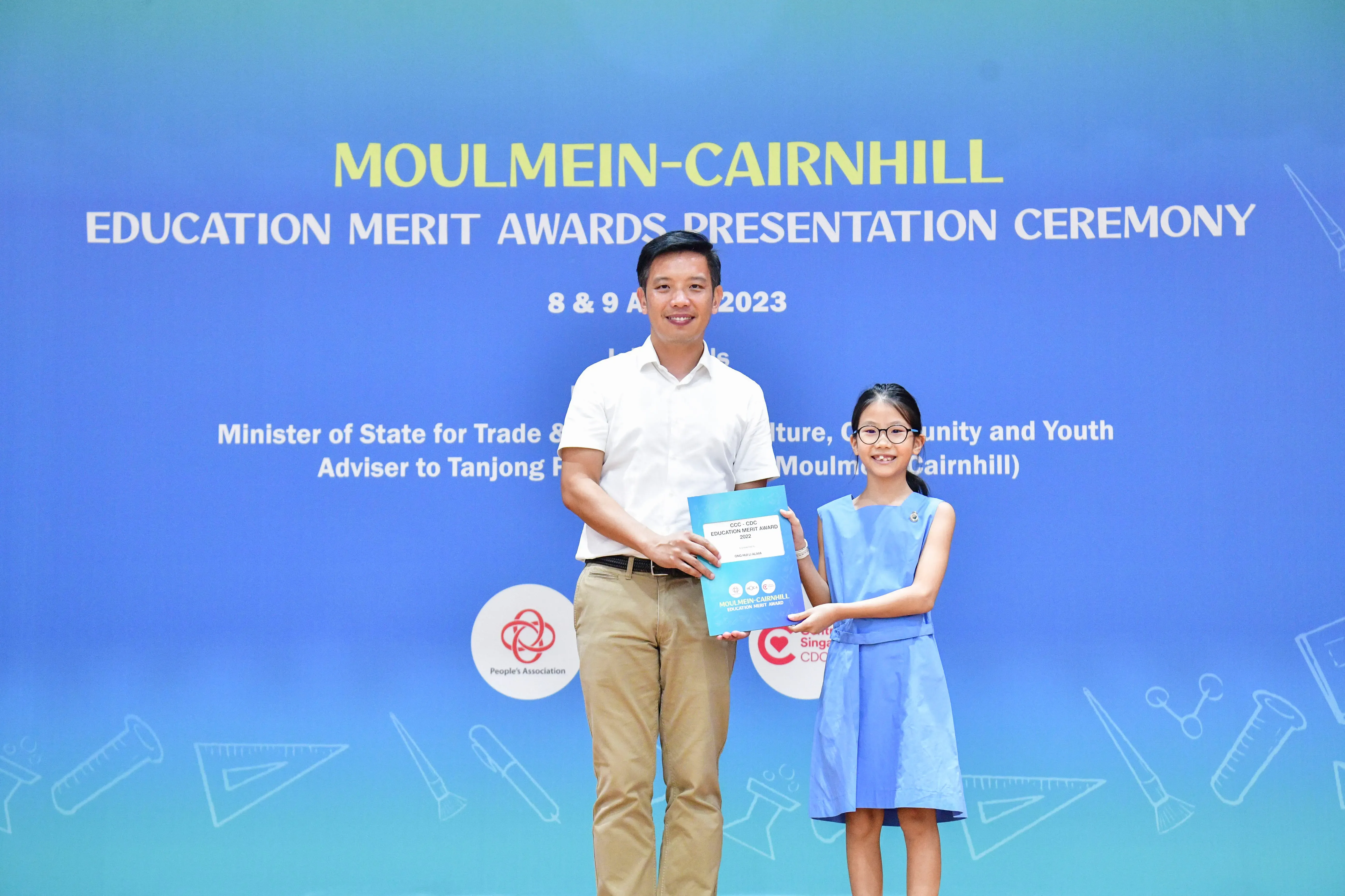 A man and a young girl hold an award certificate at the Moulmein-Cairnhill Education Merit Awards Ceremony 2023.