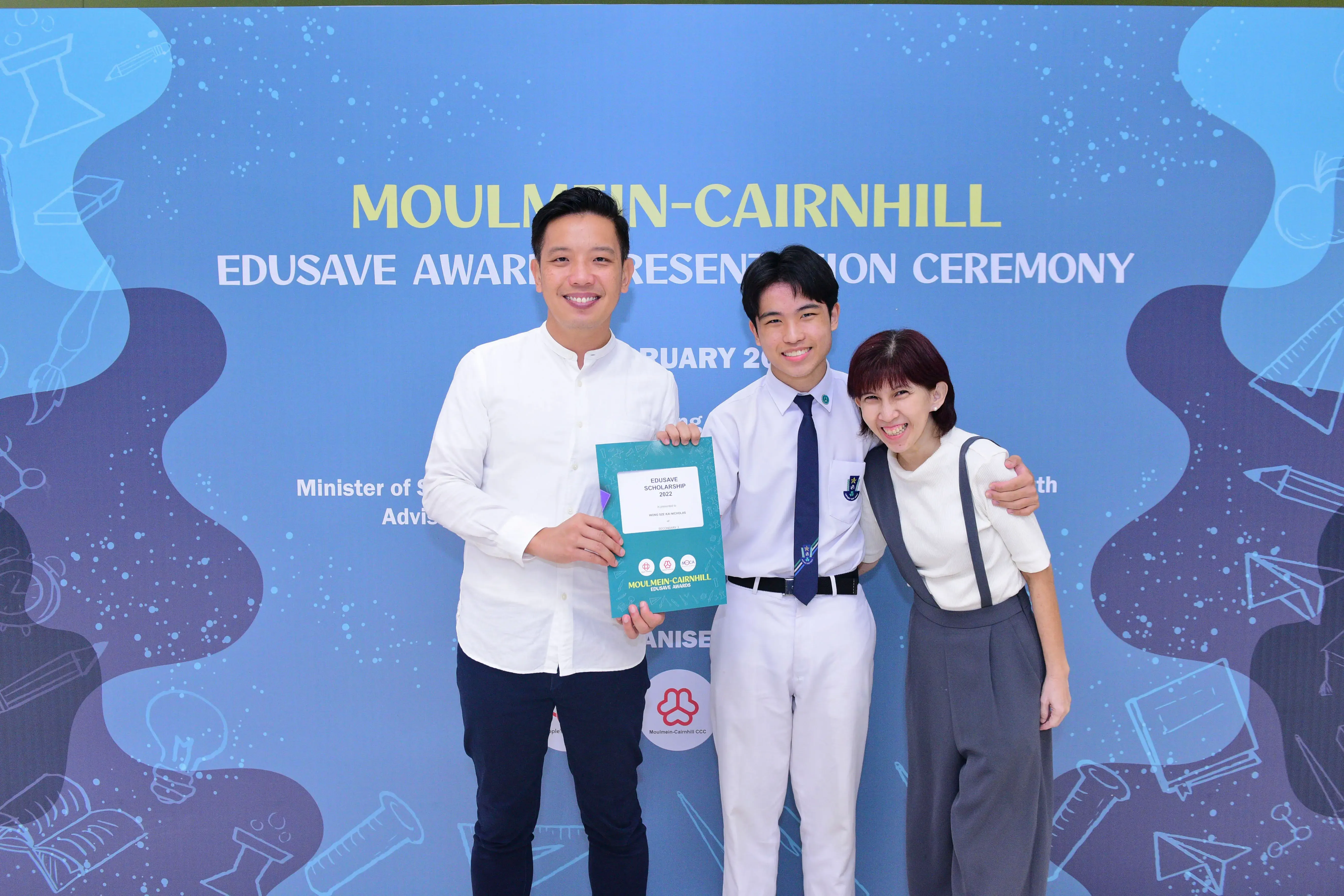 Three smiling people pose holding an Edusave Scholarship certificate at the Moulmein-Cairnhill Award Presentation Ceremony.