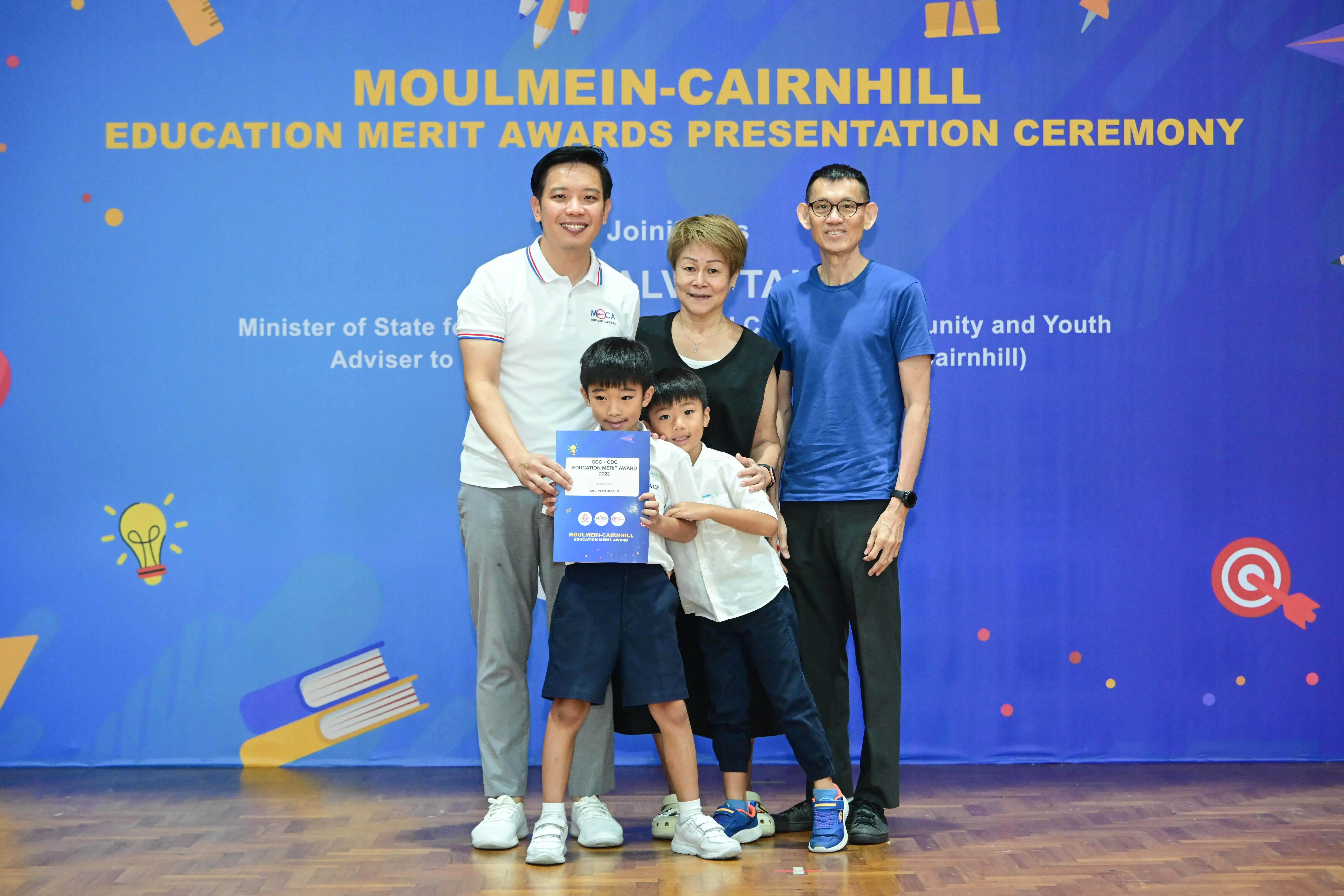 Family of five posing with an award certificate at the Moulmein-Cairnhill Education Merit Awards Presentation Ceremony.