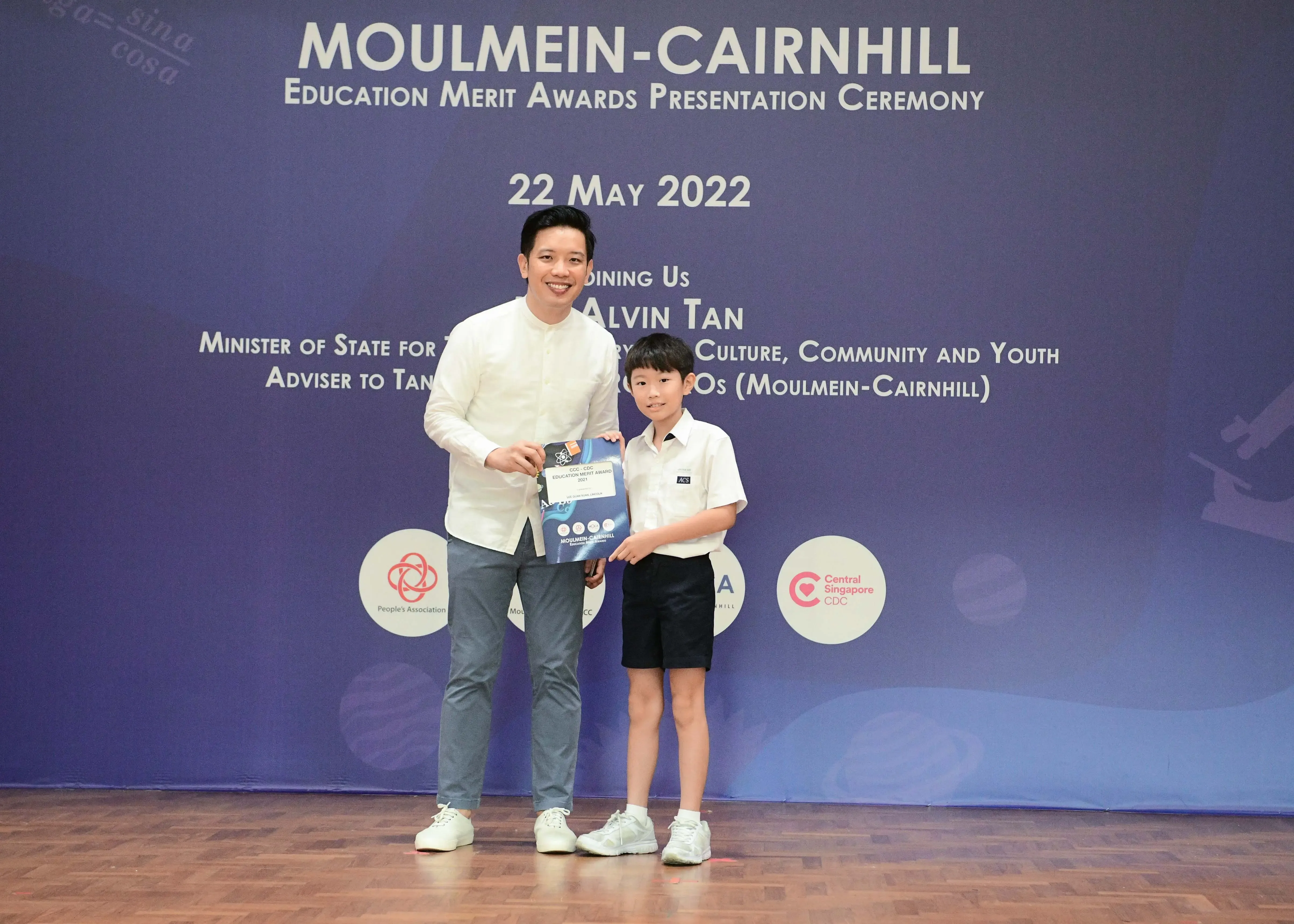 An adult and a young boy pose holding an award at the Moulmein-Cairnhill Education Merit Awards Ceremony on 22 May 2022.