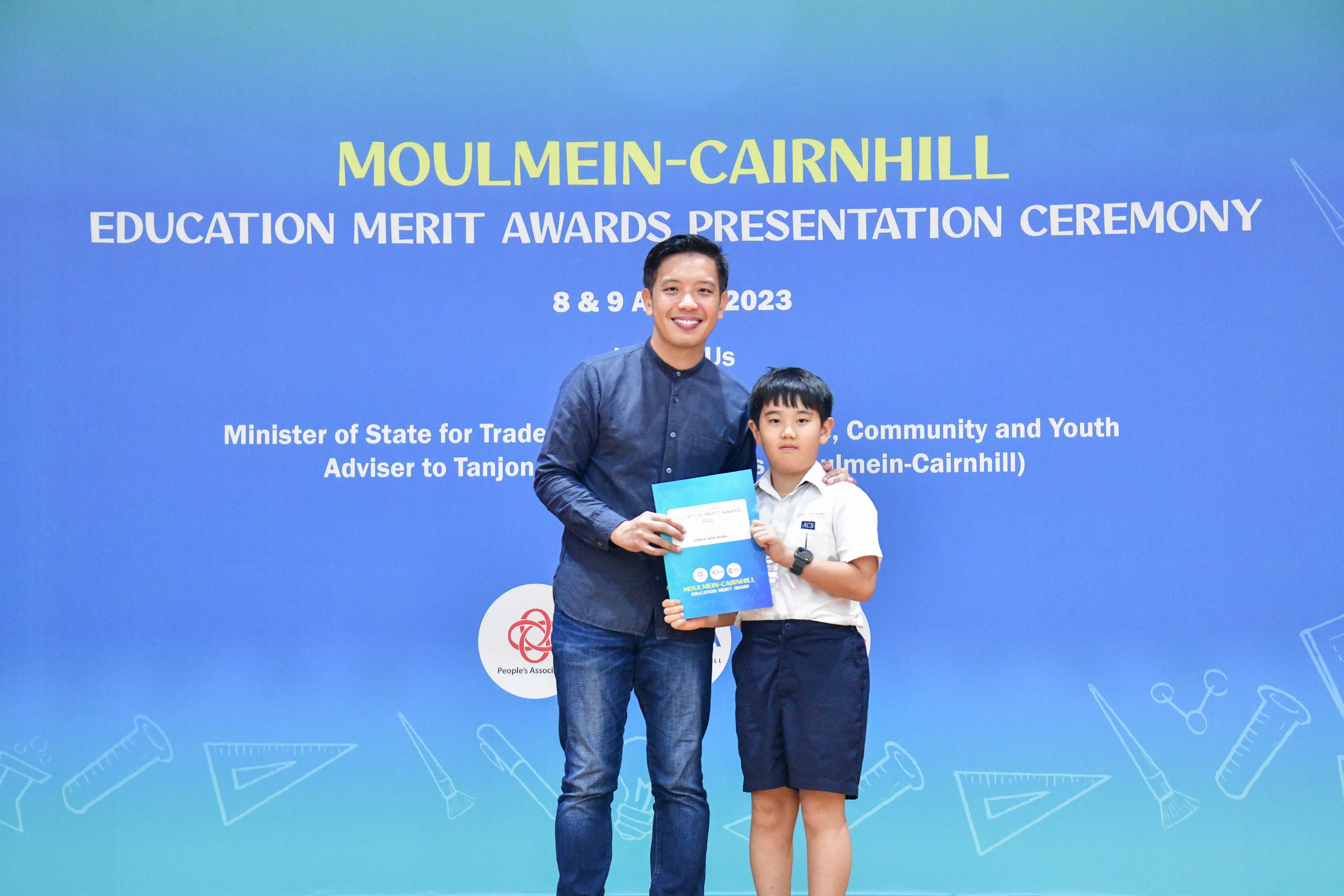 A man and a young boy hold an award certificate together at the Moulmein-Cairnhill Education Merit Awards ceremony in 2023.
