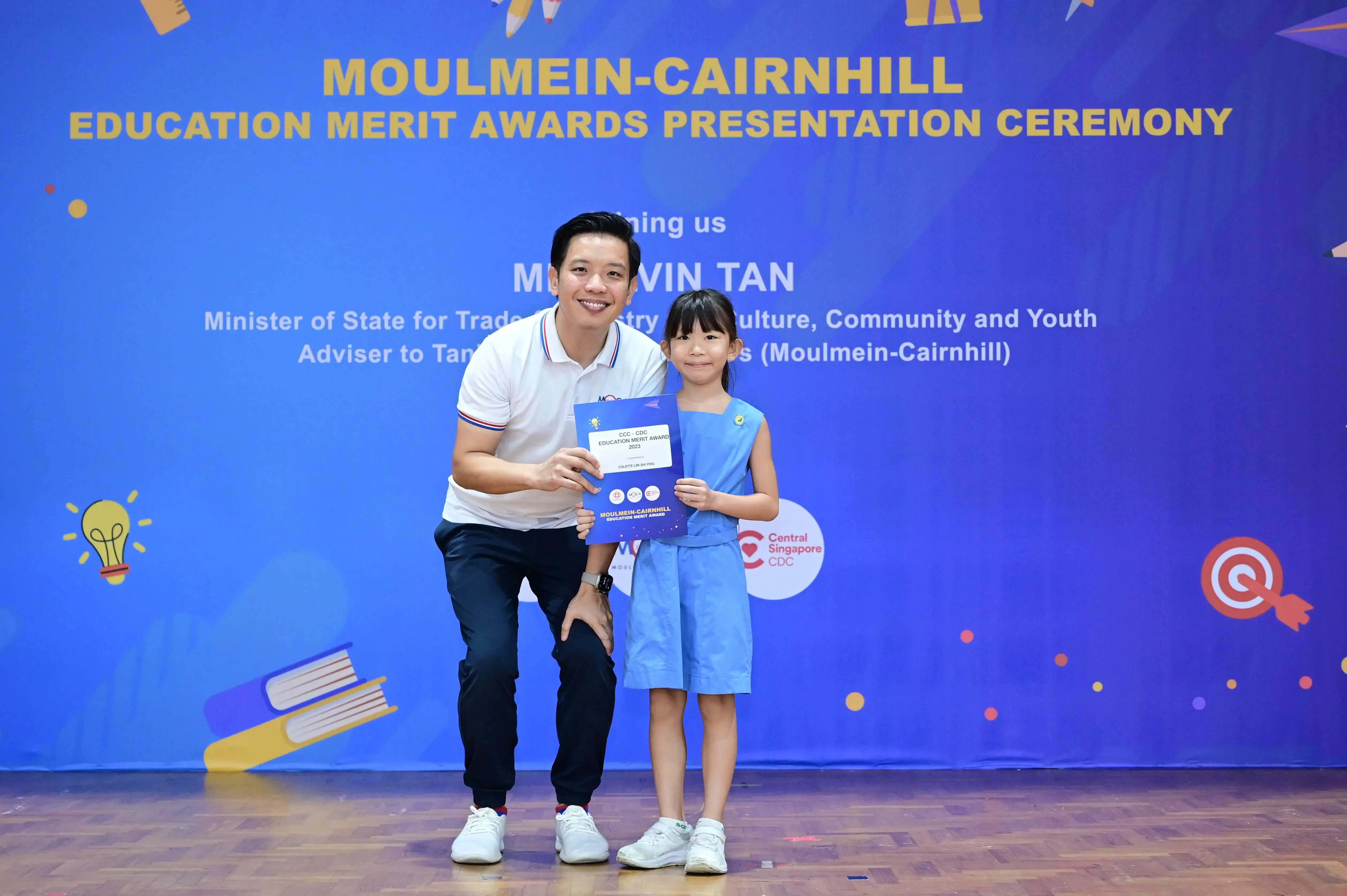 A man and a young girl hold a certificate together at the Moulmein-Cairnhill Education Merit Awards Presentation Ceremony.