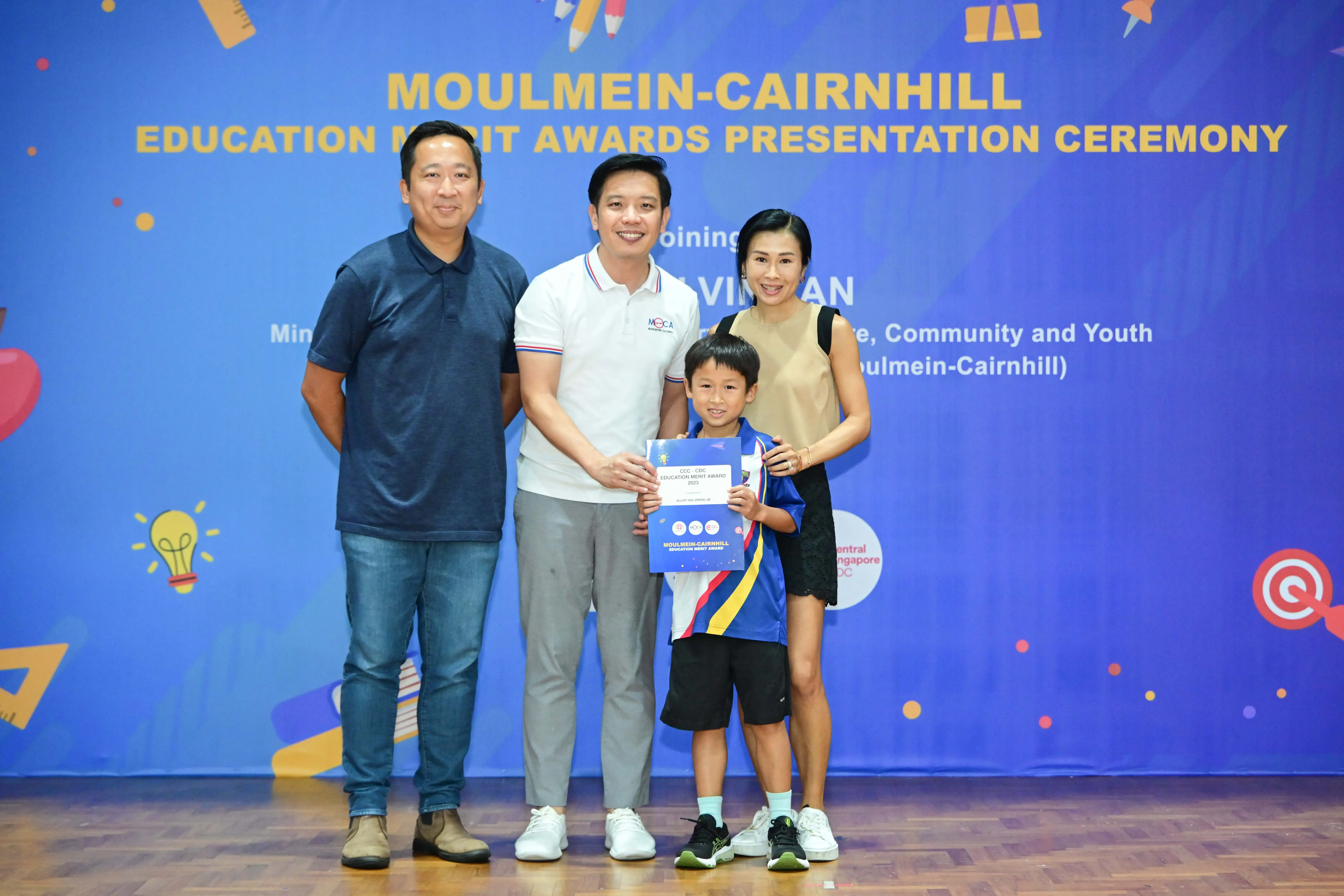 Three adults and a boy holding a certificate pose at the Moulmein-Cairnhill Education Merit Awards ceremony.