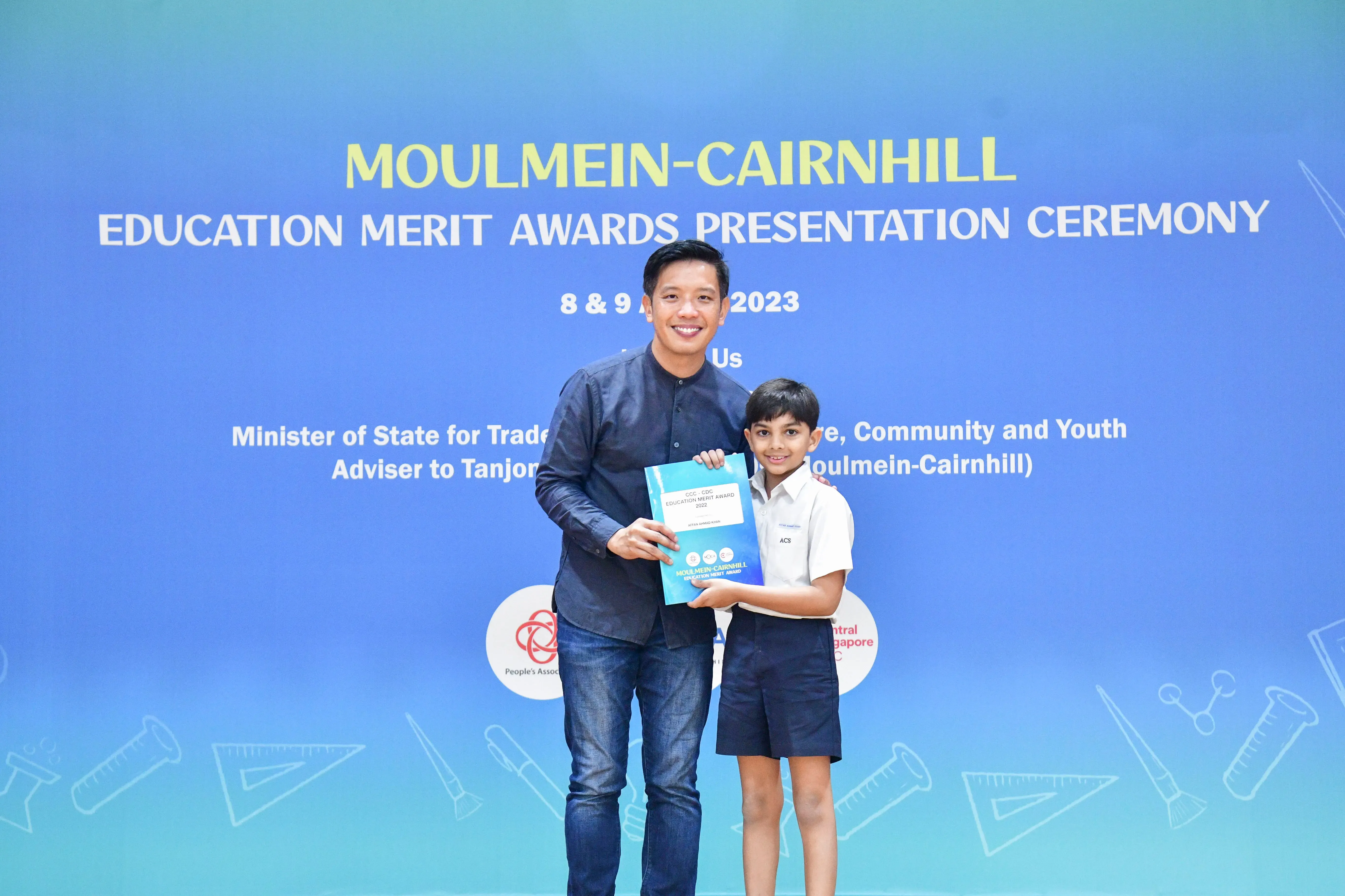 A man and a young boy hold an award certificate at the Moulmein-Cairnhill Education Merit Awards Ceremony 2023.