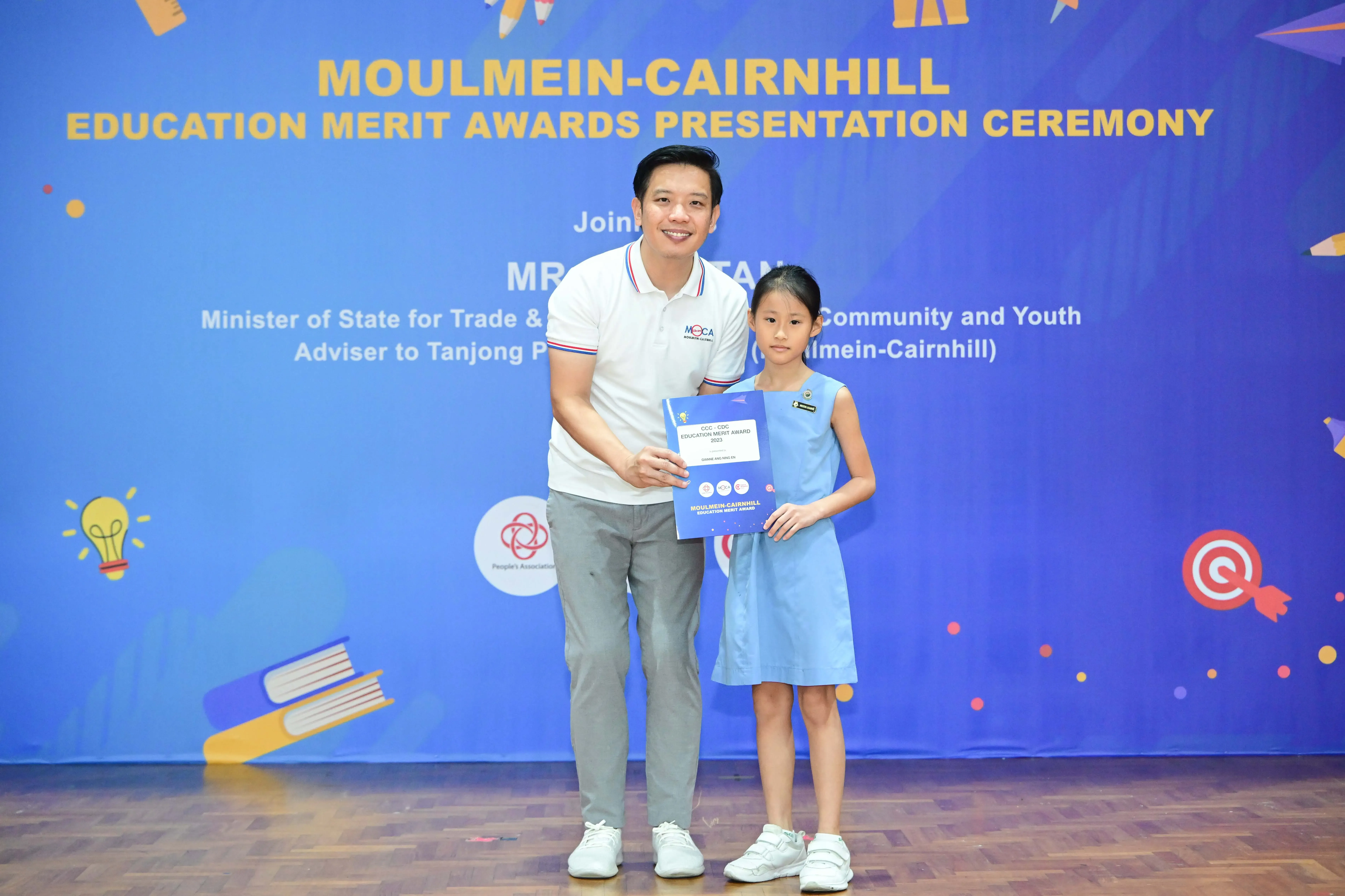 A man and a young girl hold an award certificate at the Moulmein-Cairnhill Education Merit Awards Presentation Ceremony.