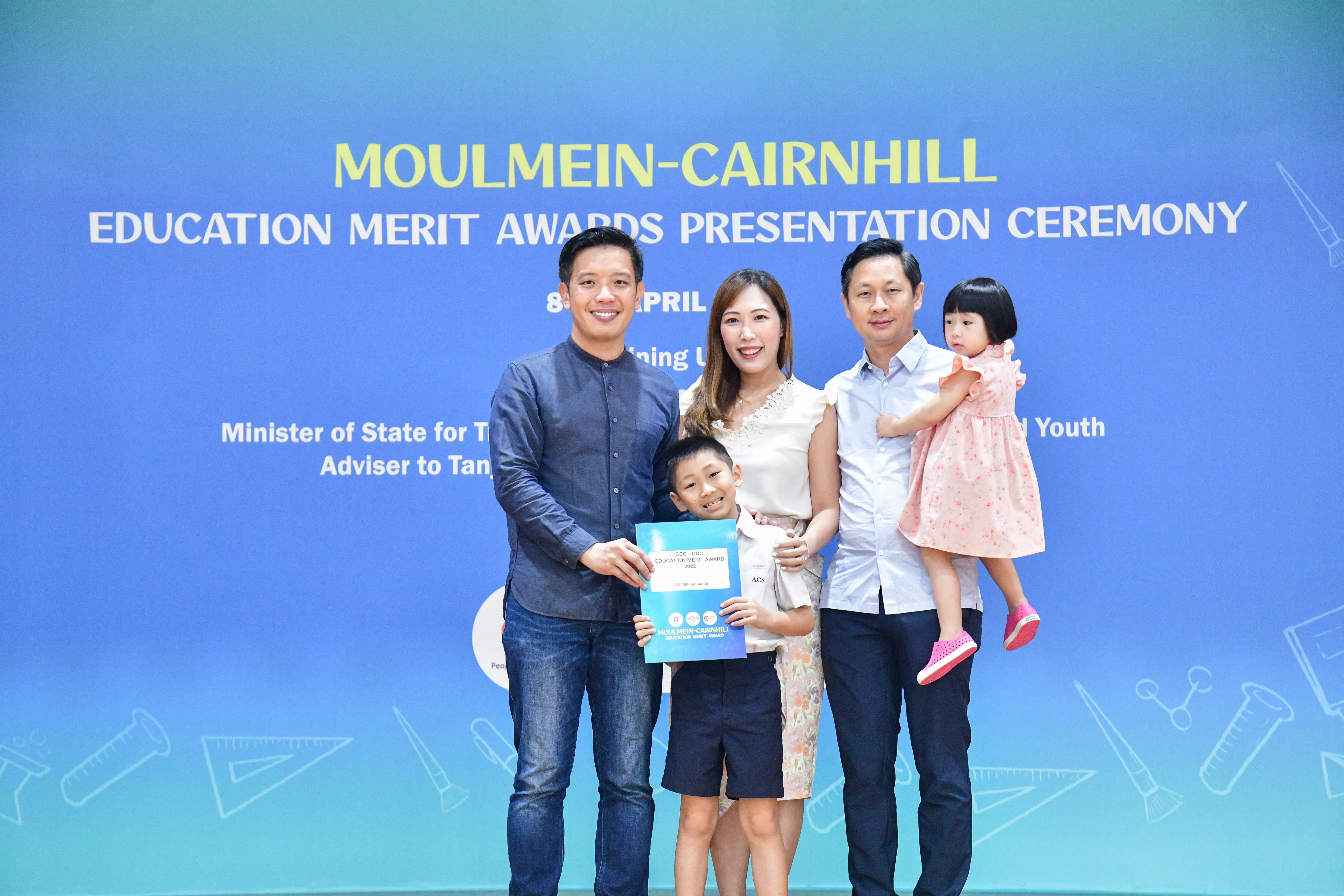 Four adults and two children pose with a certificate at the Moulmein-Cairnhill Education Merit Awards Presentation Ceremony.