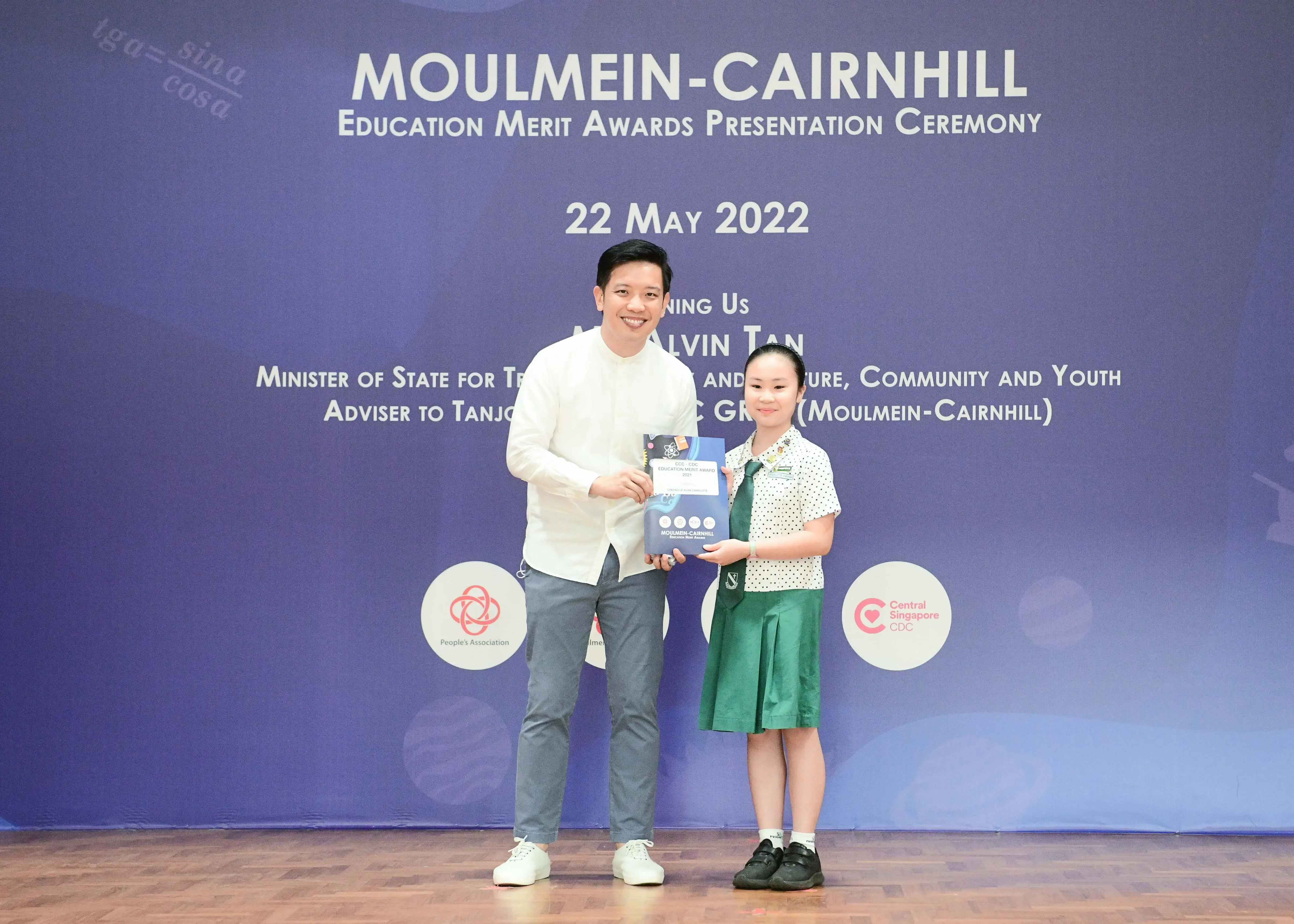 A man and a young girl in school uniform hold an award at the Moulmein-Cairnhill Education Merit Awards ceremony on 22 May 2022.