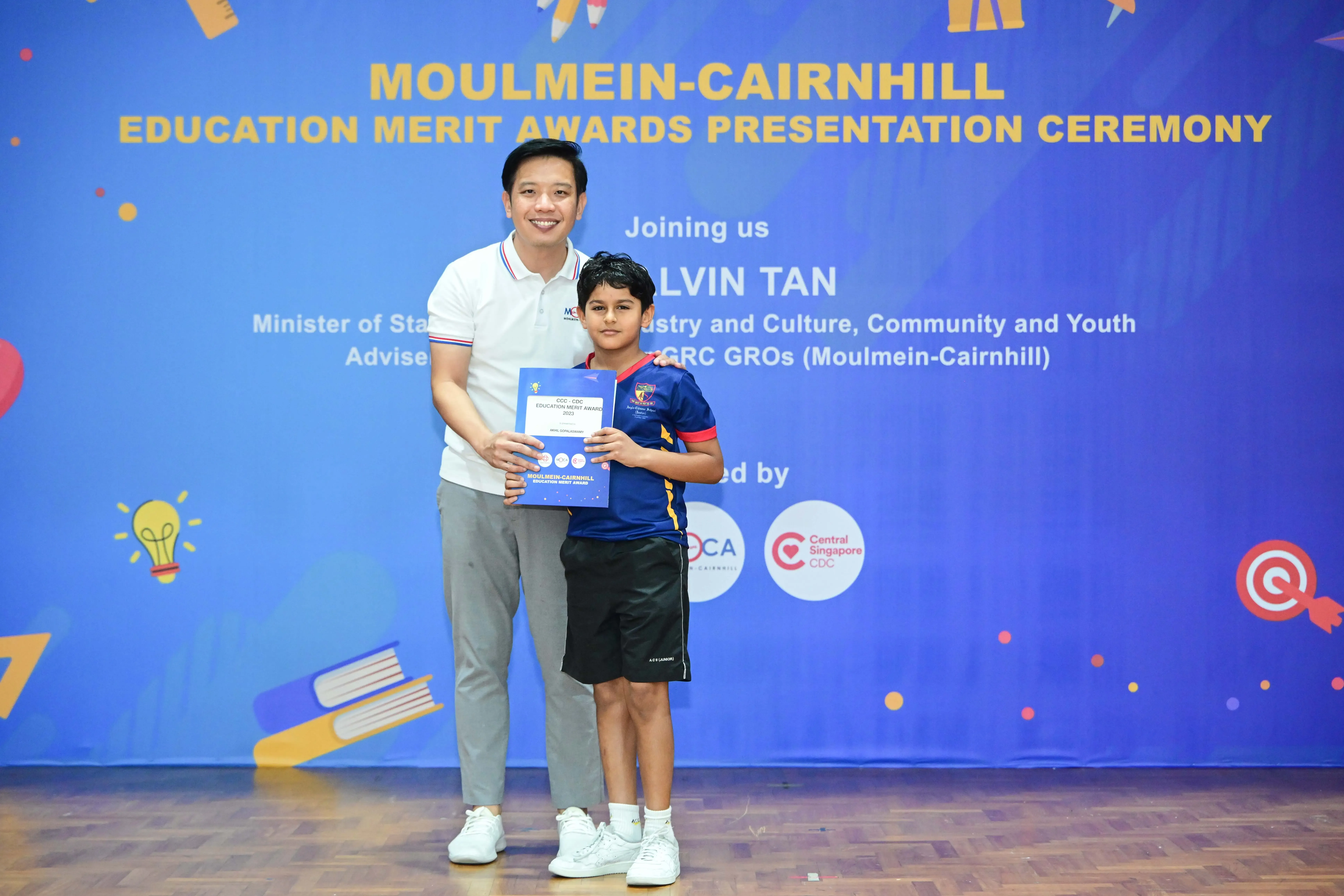 A man and a young boy hold an award certificate at the Moulmein-Cairnhill Education Merit Awards Presentation Ceremony.