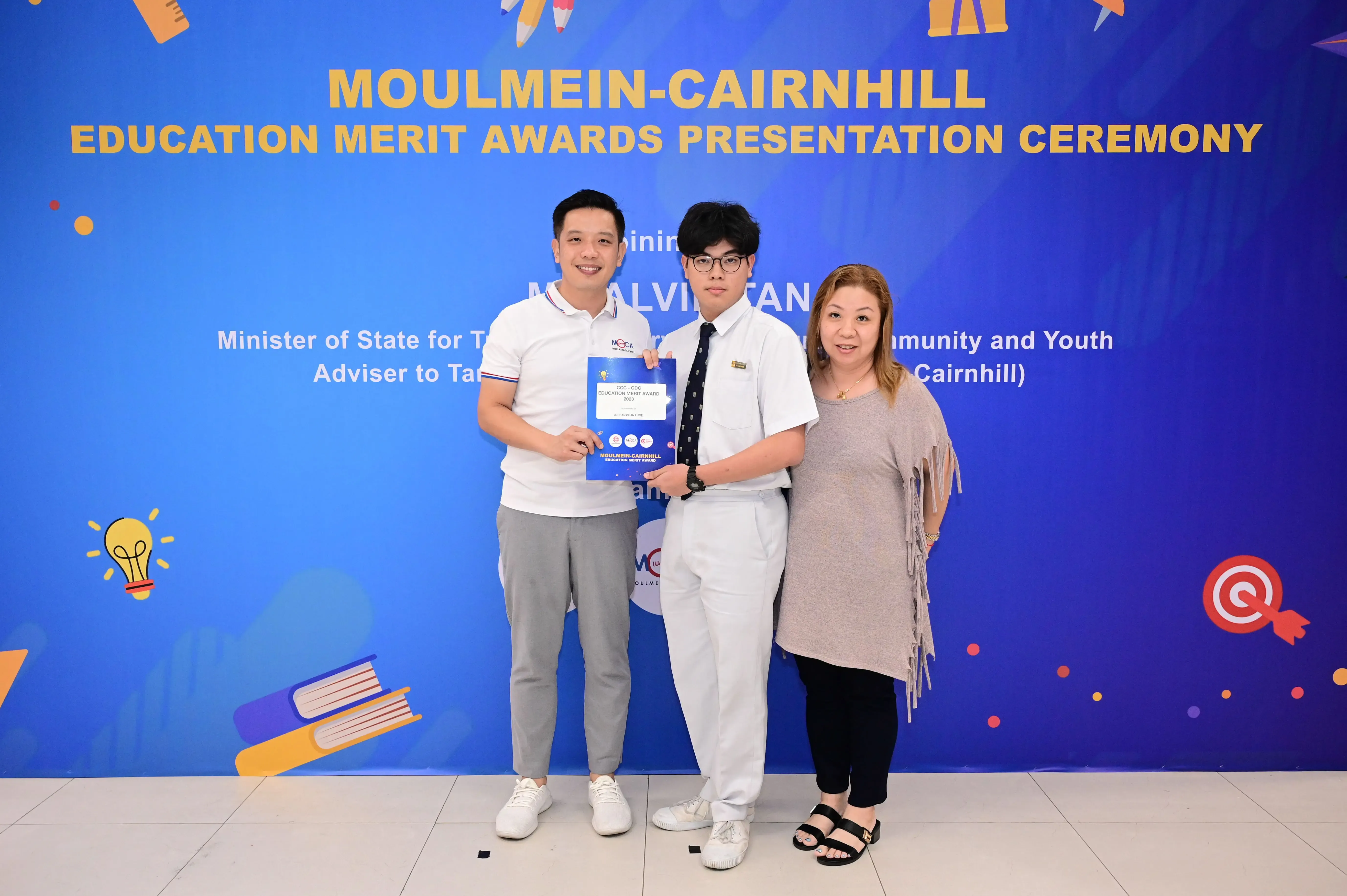 Three people pose holding a certificate at the Moulmein-Cairnhill Education Merit Awards Presentation Ceremony.
