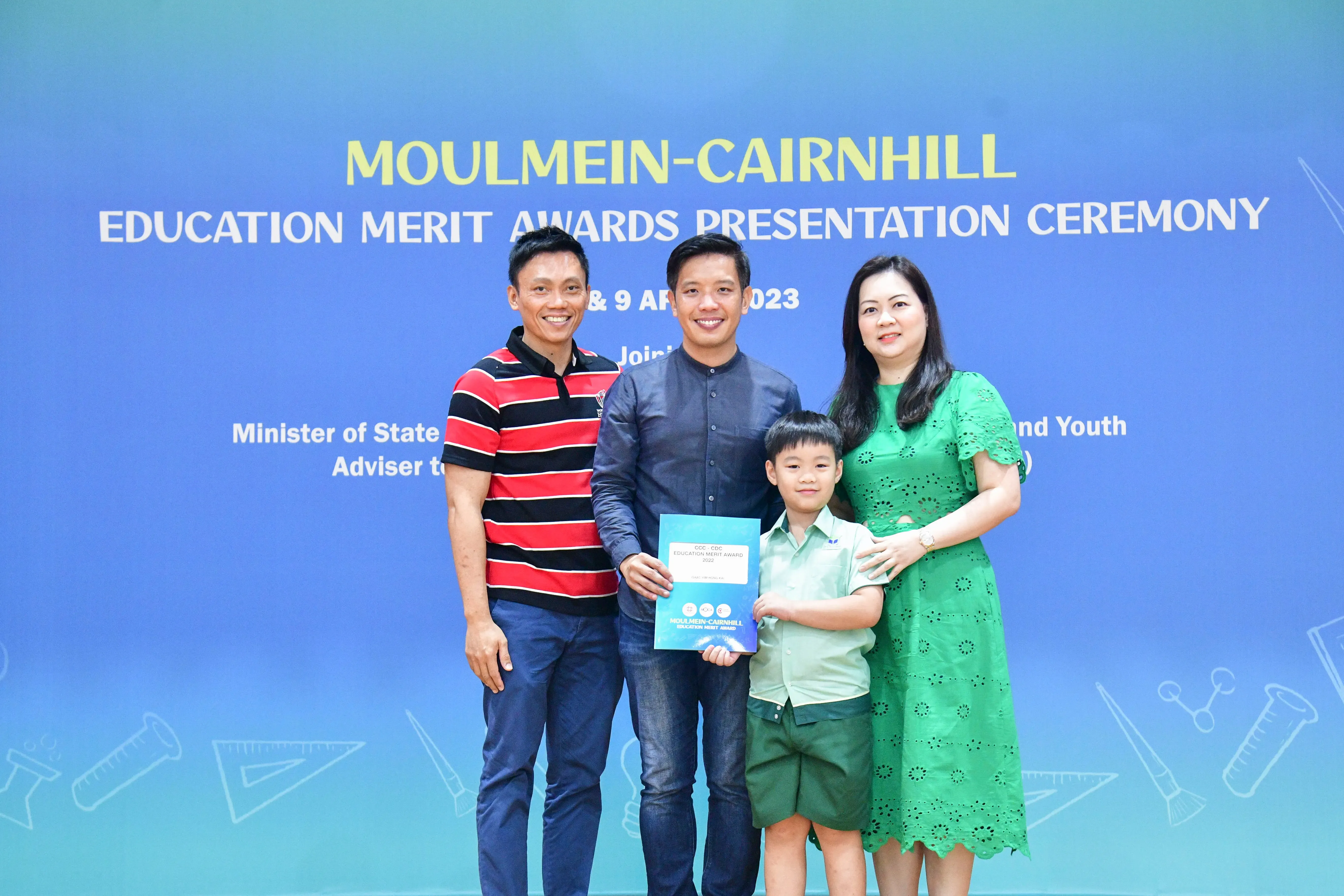 Three adults and a young boy pose holding an award certificate at the Moulmein-Cairnhill Education Merit Awards 2023.
