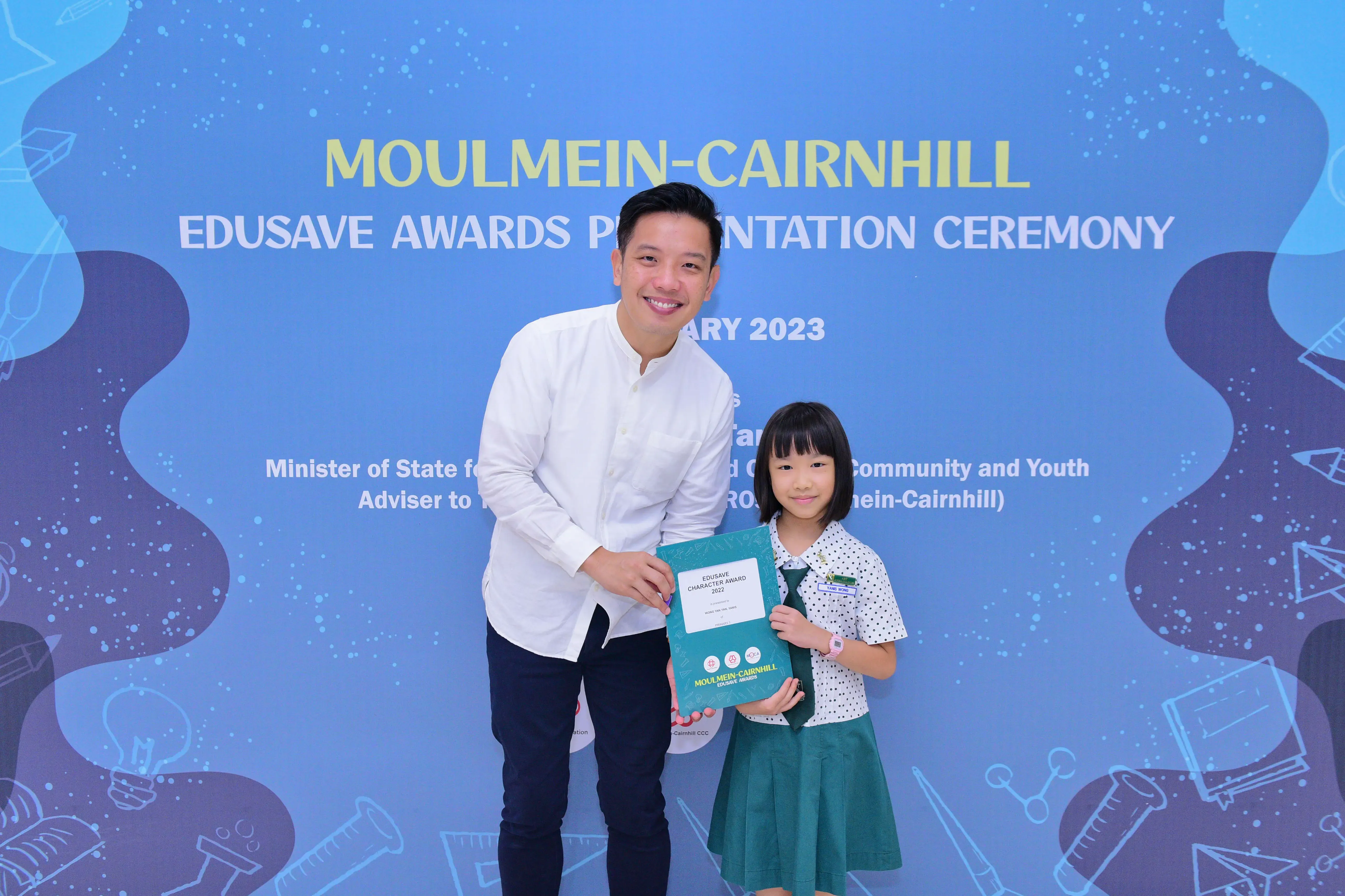 A man and a young girl hold an Edusave Character Award at the Moulmein-Cairnhill Edusave Awards Ceremony 2023.