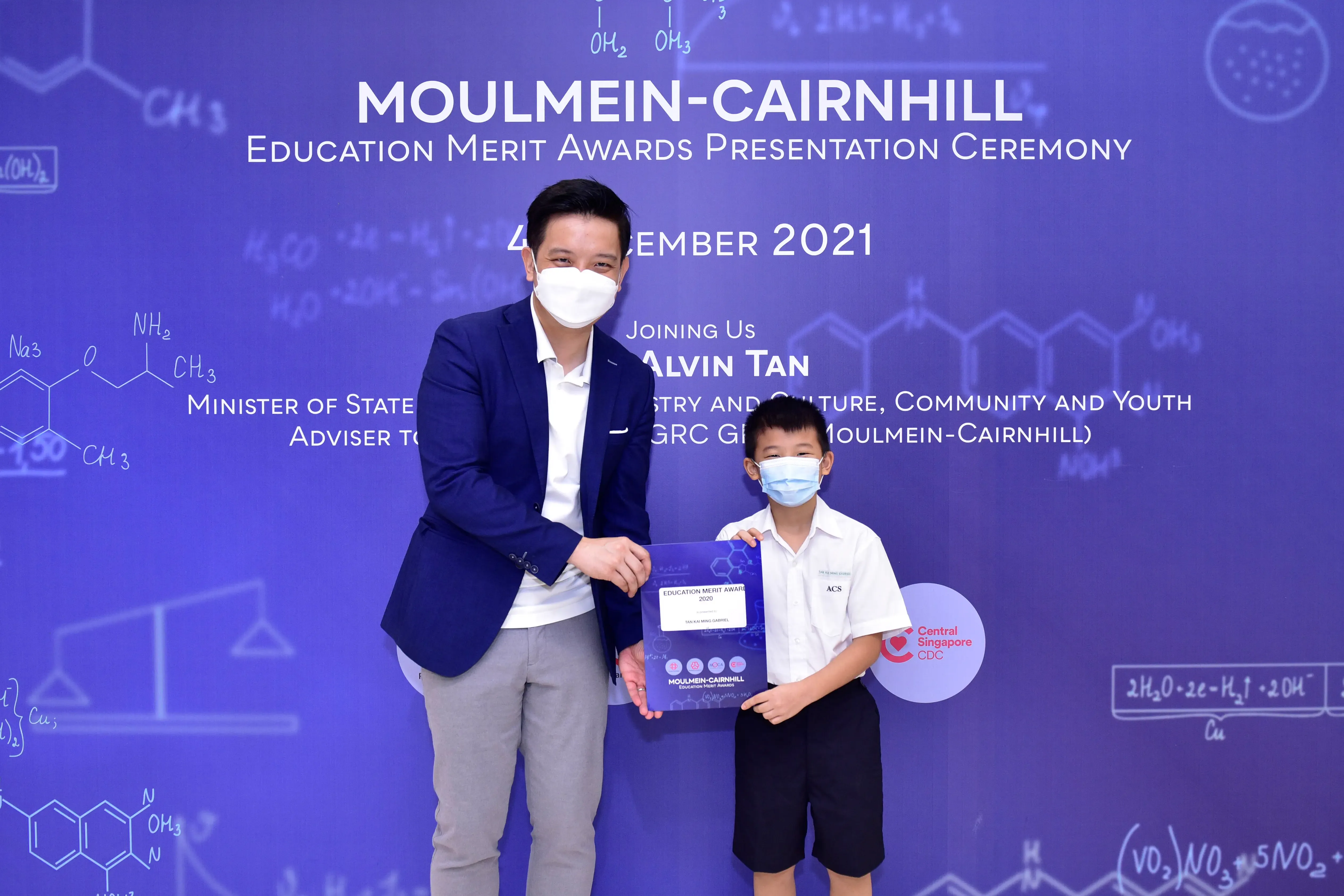 An adult and a young boy, both masked, hold an award certificate at the Moulmein-Cairnhill Education Merit Awards 2021.