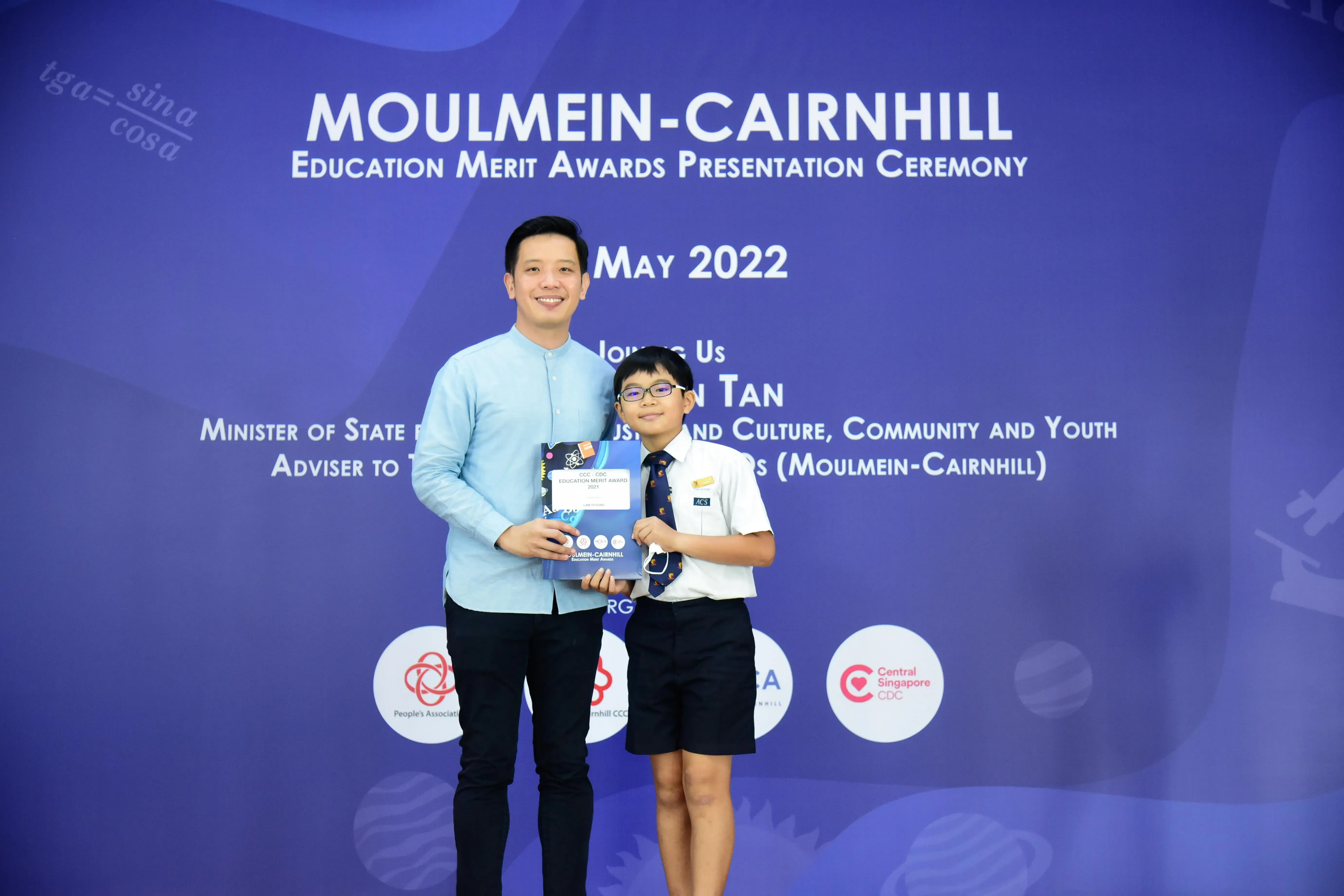 Adult and uniformed schoolboy holding an award at the Moulmein-Cairnhill Education Merit Awards Ceremony, May 2022.