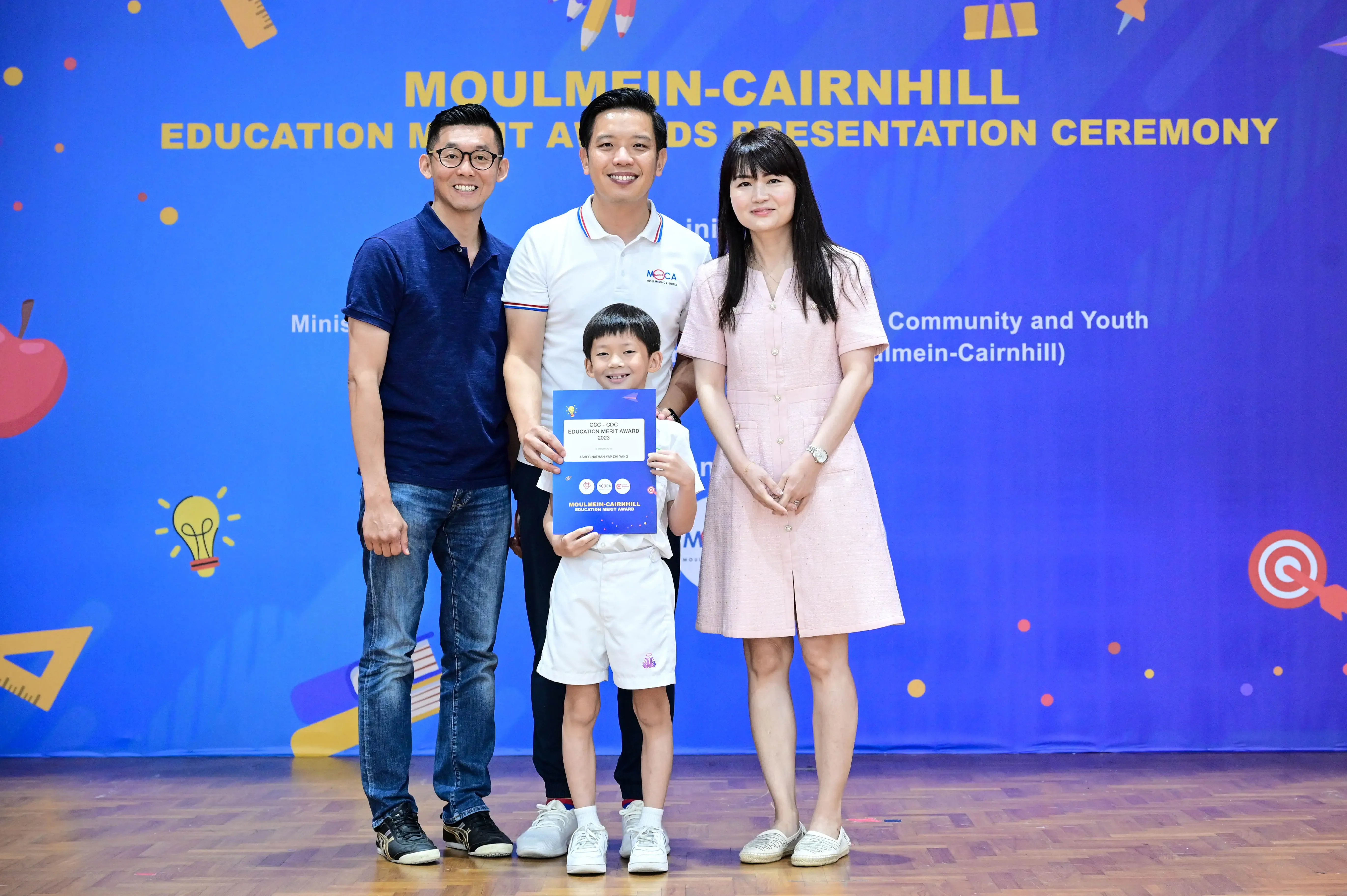 Three adults and a young boy holding a certificate pose at the Moulmein-Cairnhill Education Merit Awards Ceremony.