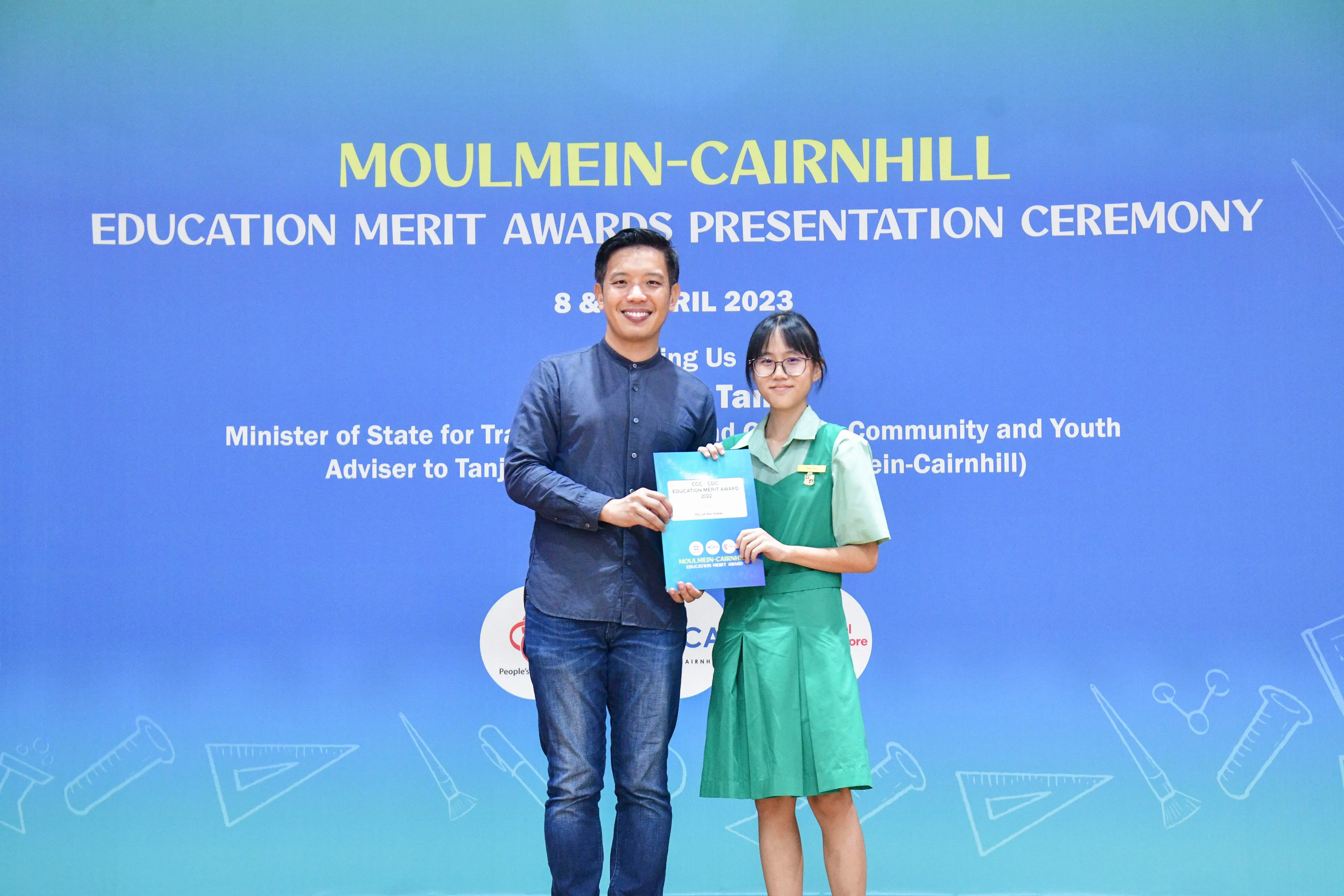 A man and a young girl in a green school uniform hold a certificate at the Moulmein-Cairnhill Education Merit Awards 2023.