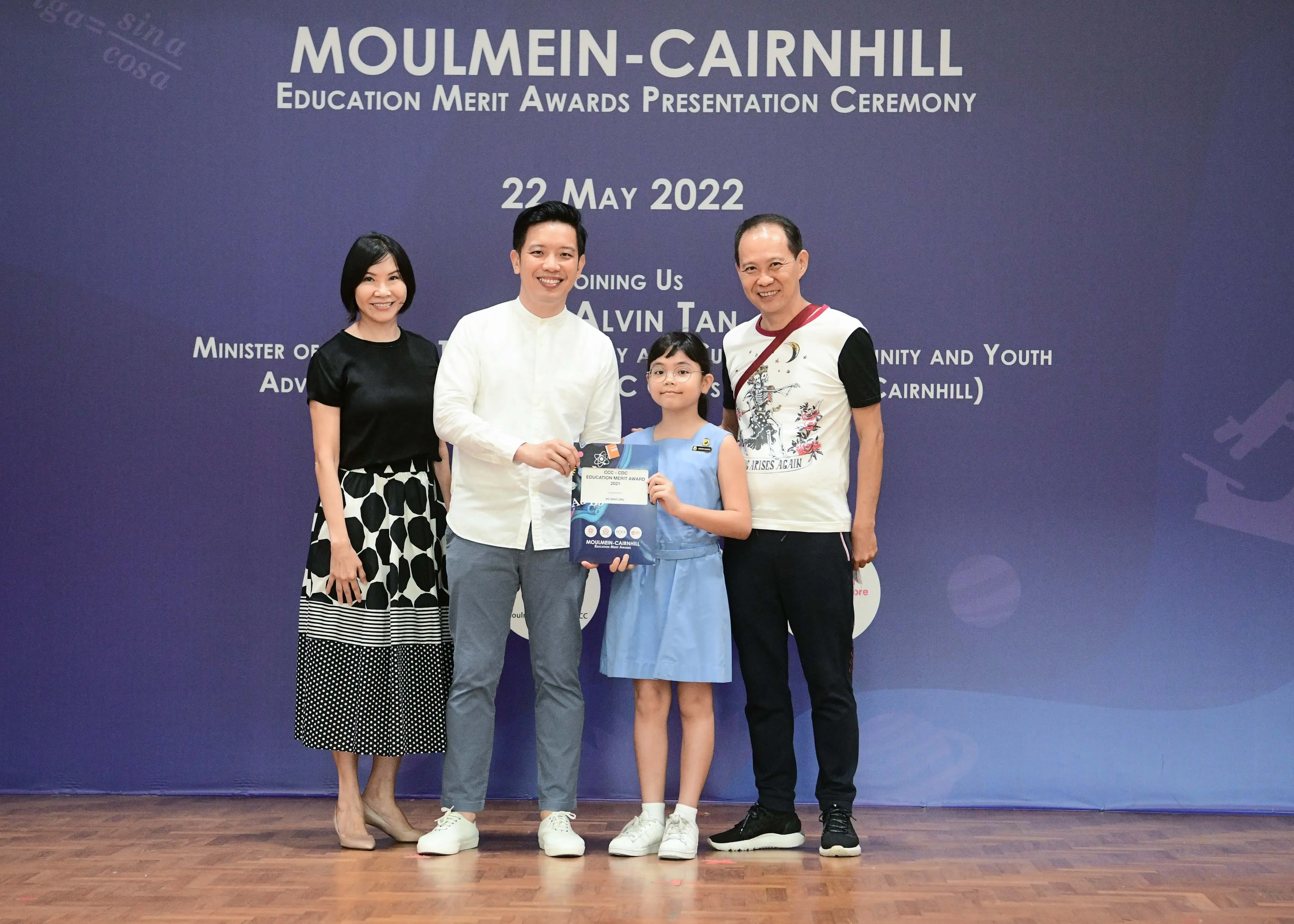 Four people pose at the Moulmein-Cairnhill Education Merit Awards ceremony on 22 May 2022, with a girl holding a certificate.