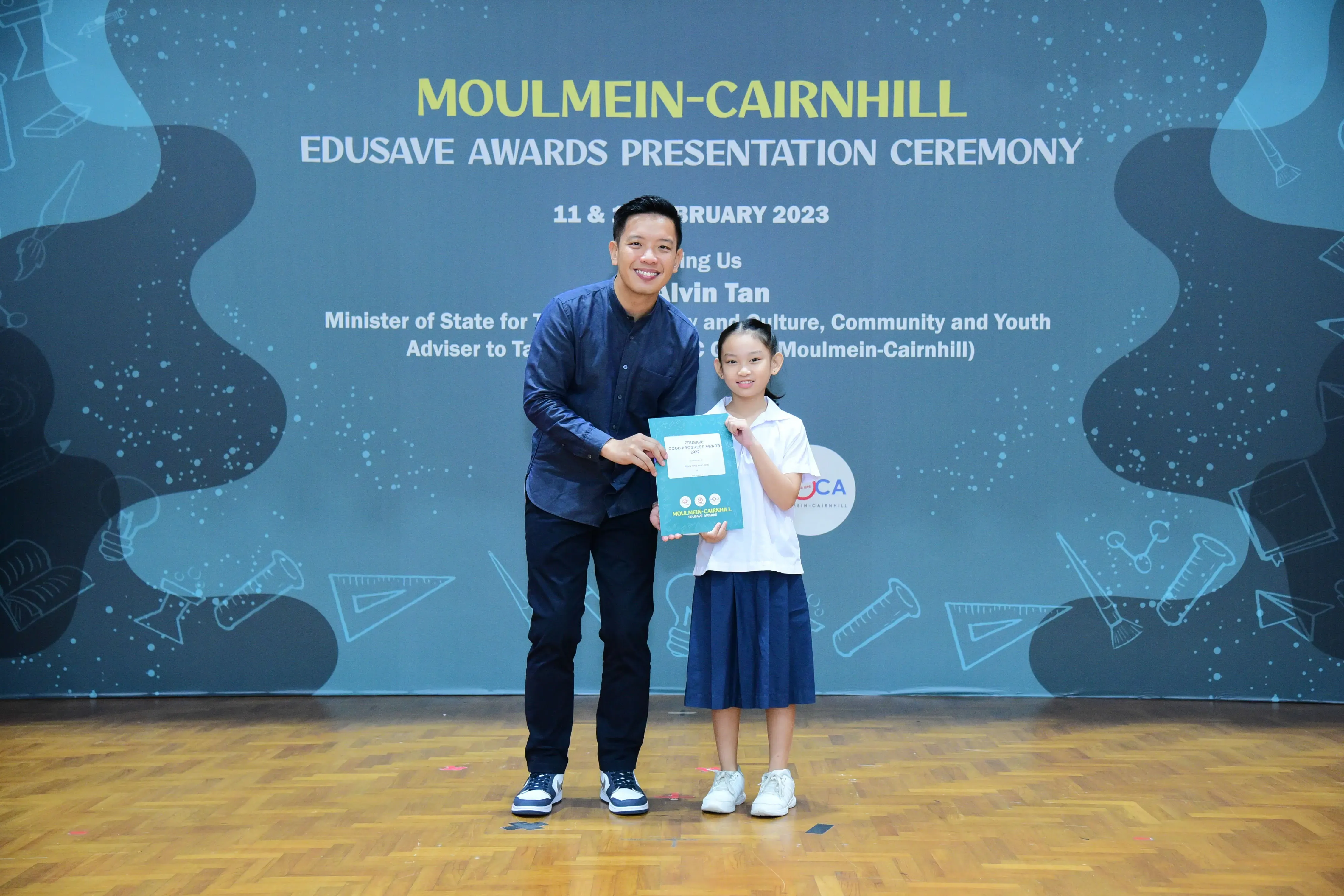 A man and a young girl hold an award booklet at the Moulmein-Cairnhill Edusave Awards Presentation Ceremony 2023.