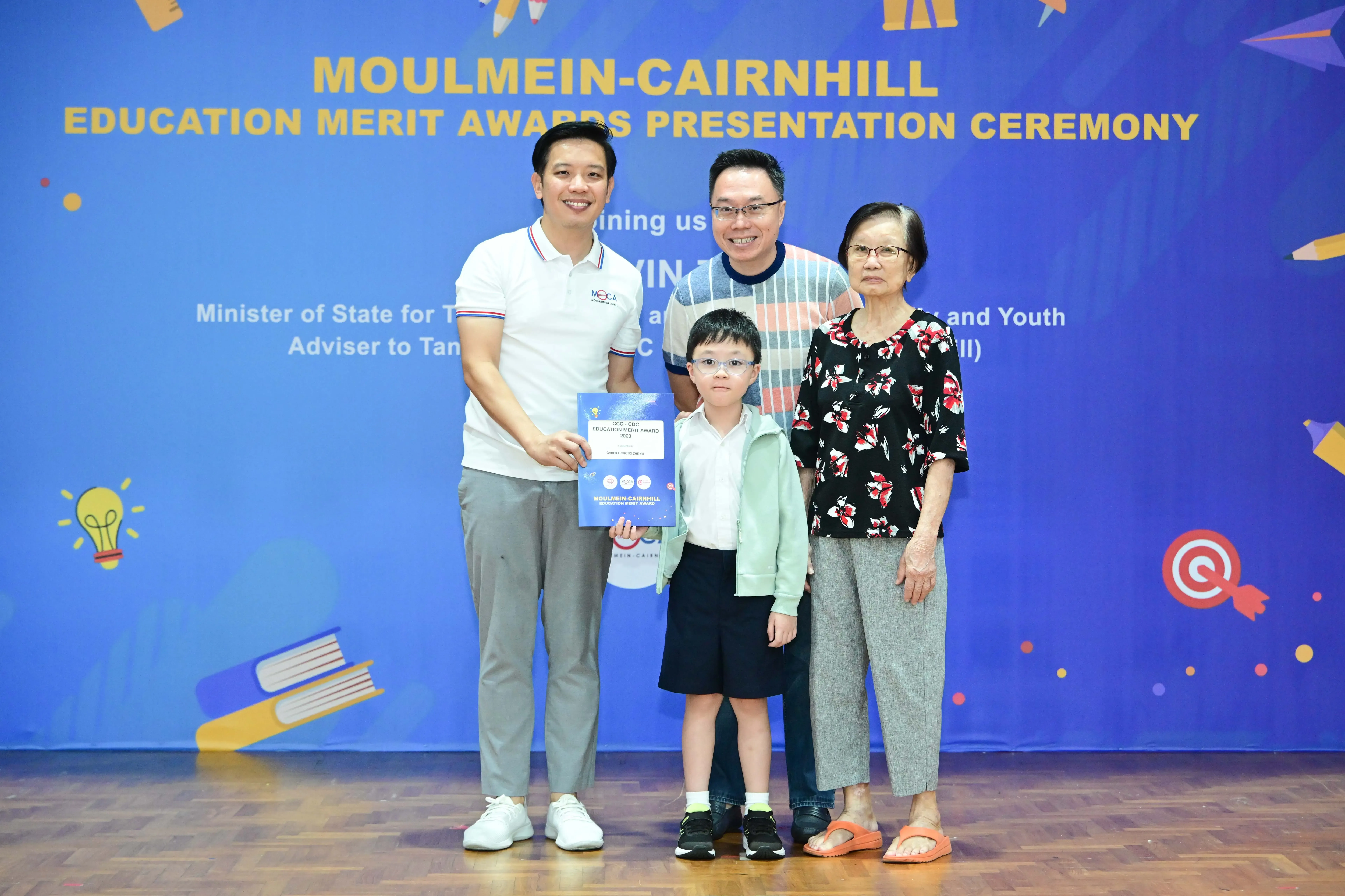 Three adults and a young boy holding a certificate pose at the Moulmein-Cairnhill Education Merit Awards ceremony.