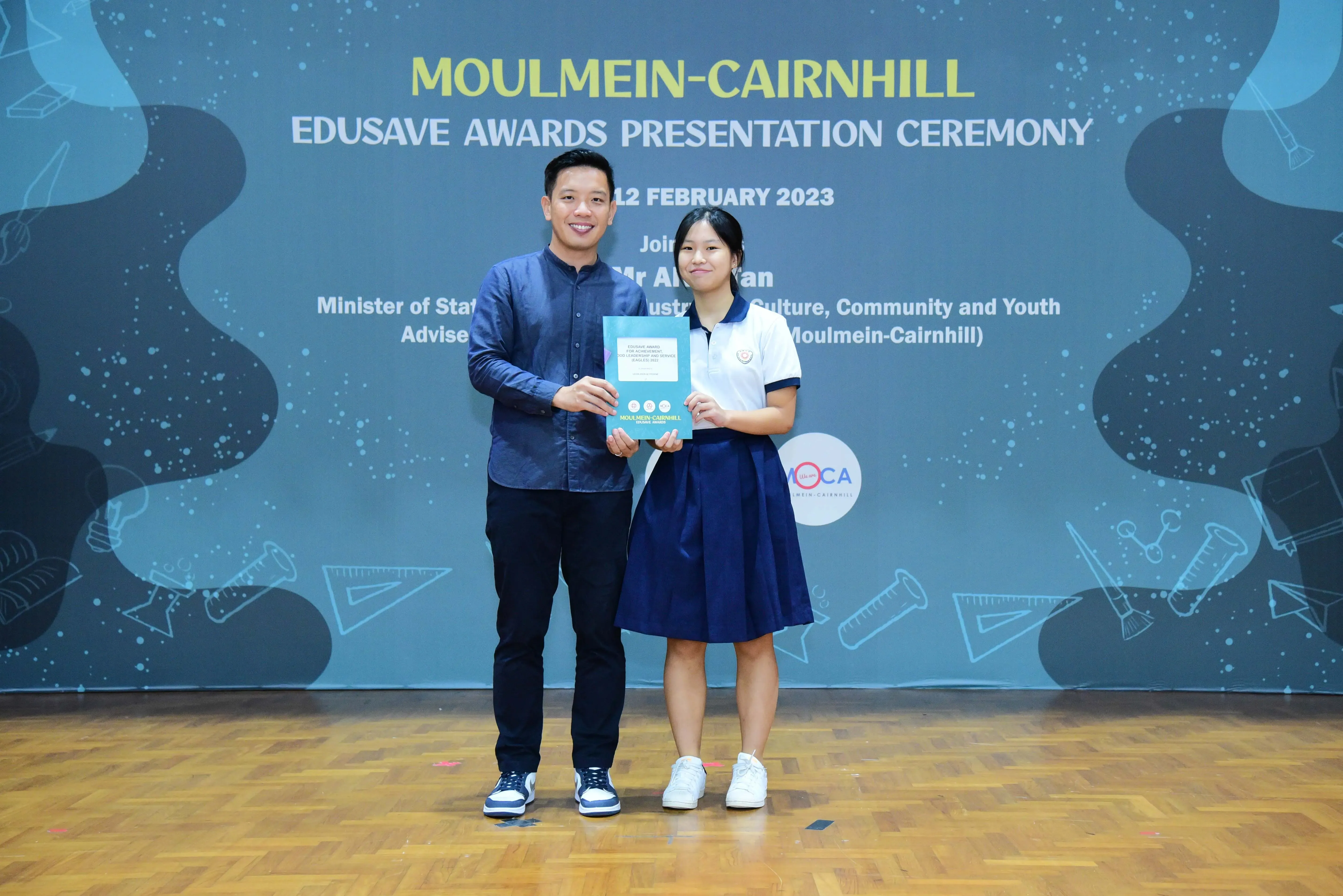Two people hold a certificate together at the Moulmein-Cairnhill Edusave Awards Presentation Ceremony on 12 February 2023.