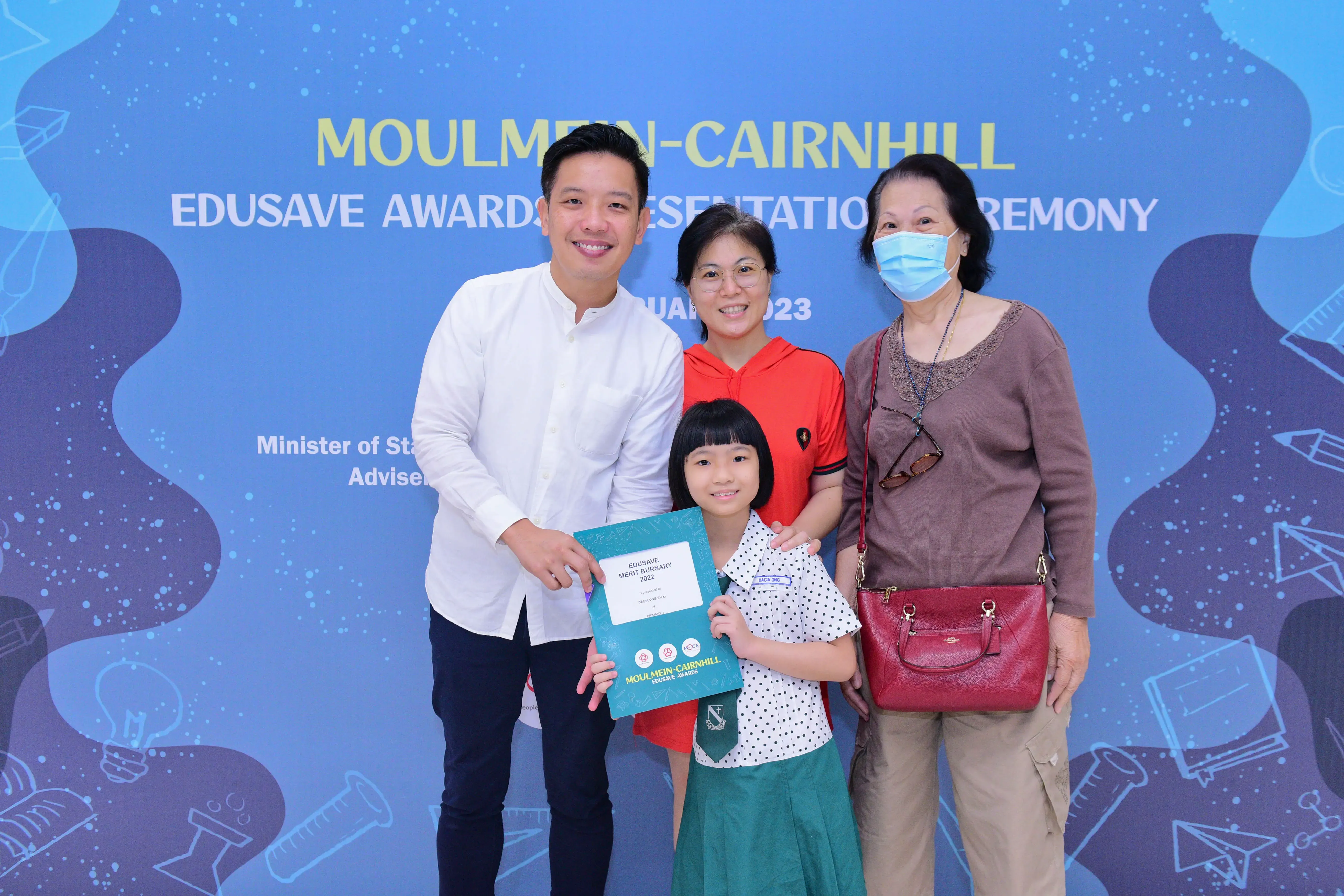 A young girl holds a certificate with three adults at the Moulmein-Cairnhill Edusave Awards Ceremony 2023.