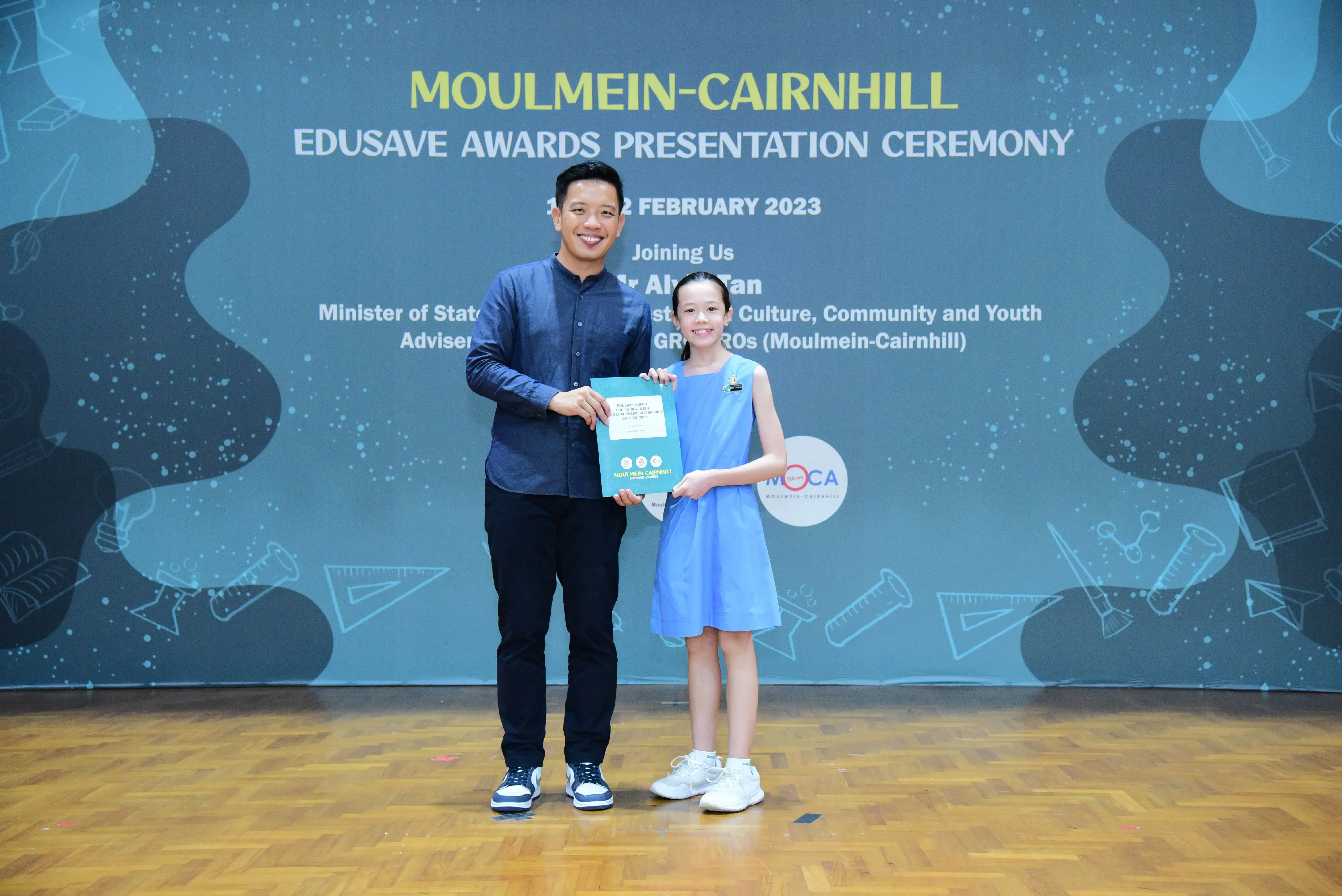 A man and a young girl hold a certificate together at the Moulmein-Cairnhill Edusave Awards Presentation Ceremony 2023.