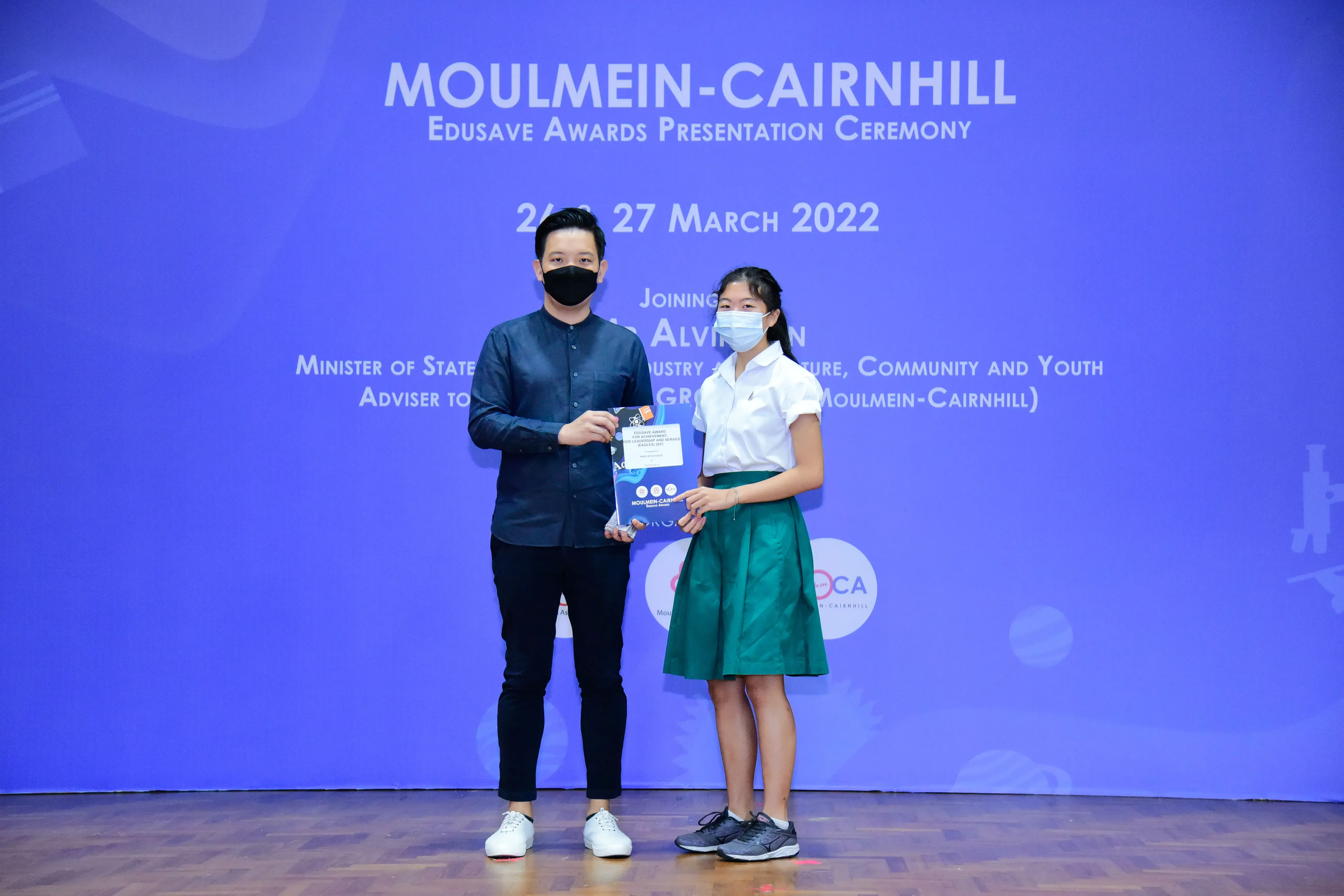 Two masked individuals hold an award at the Moulmein-Cairnhill Edusave Awards Presentation Ceremony, March 2022.