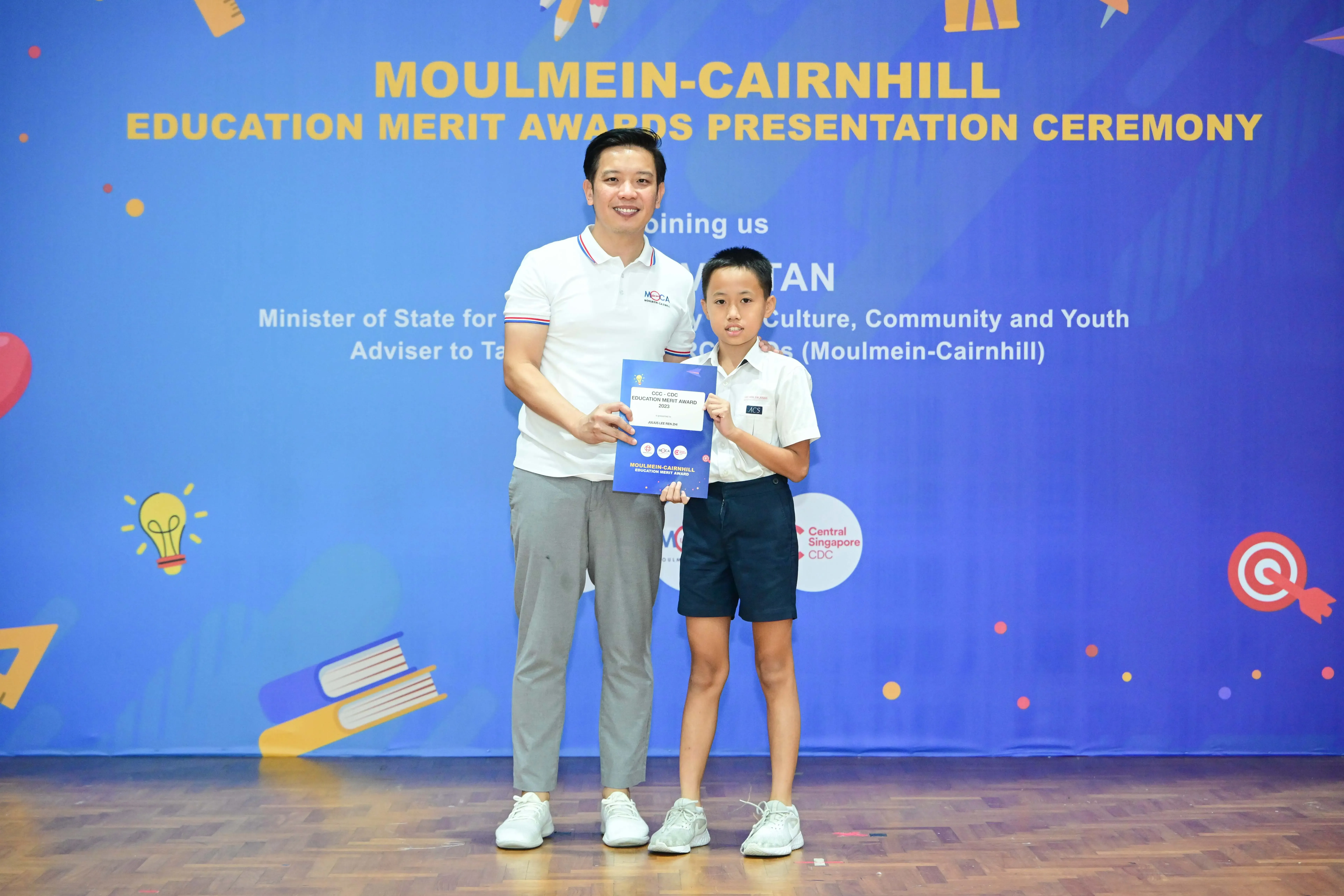 Man and young boy hold an award certificate at the Moulmein-Cairnhill Education Merit Awards Presentation Ceremony.