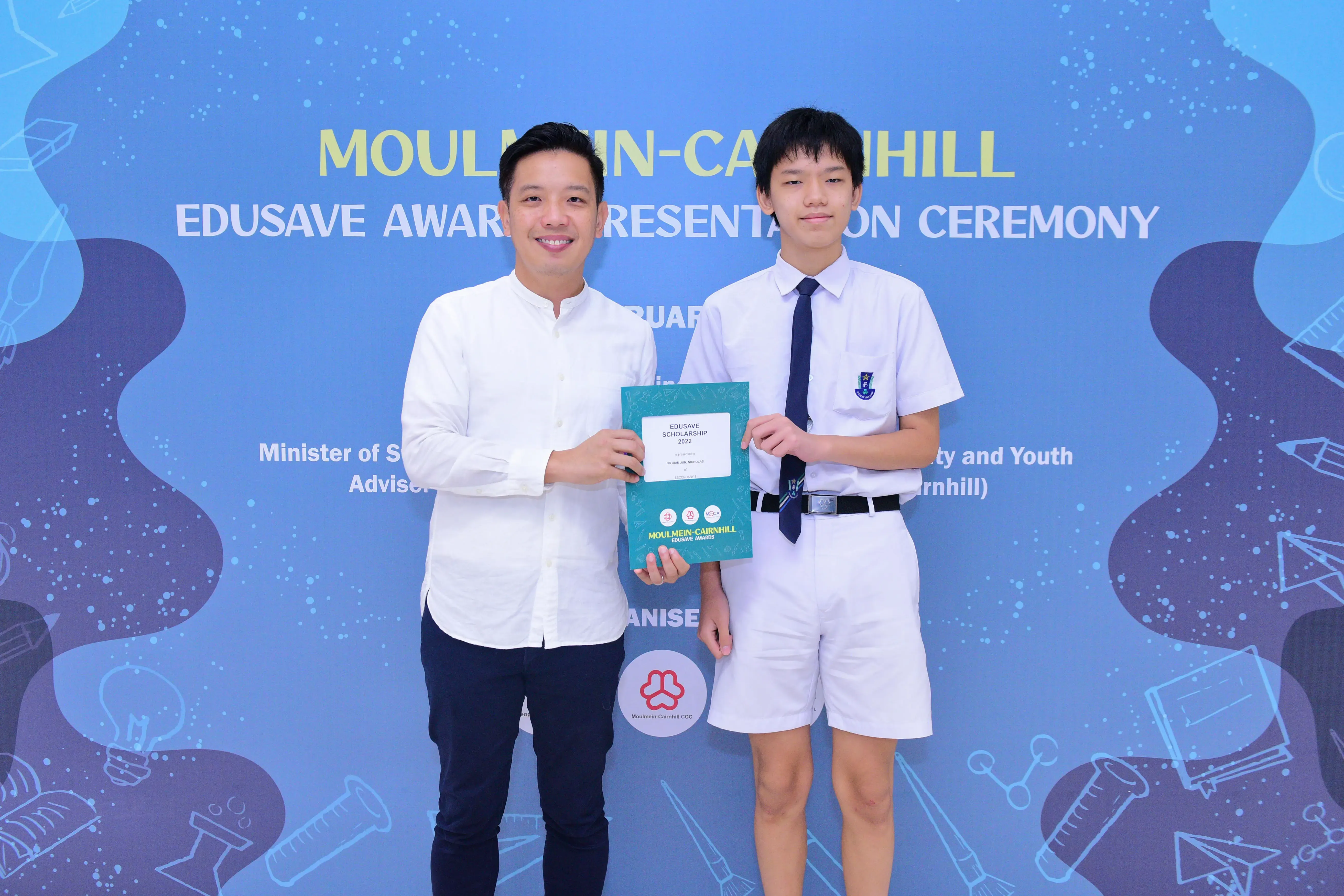 Two men pose holding an Edusave Scholarship certificate at the Moulmein-Cairnhill Edusave Awards Presentation Ceremony.