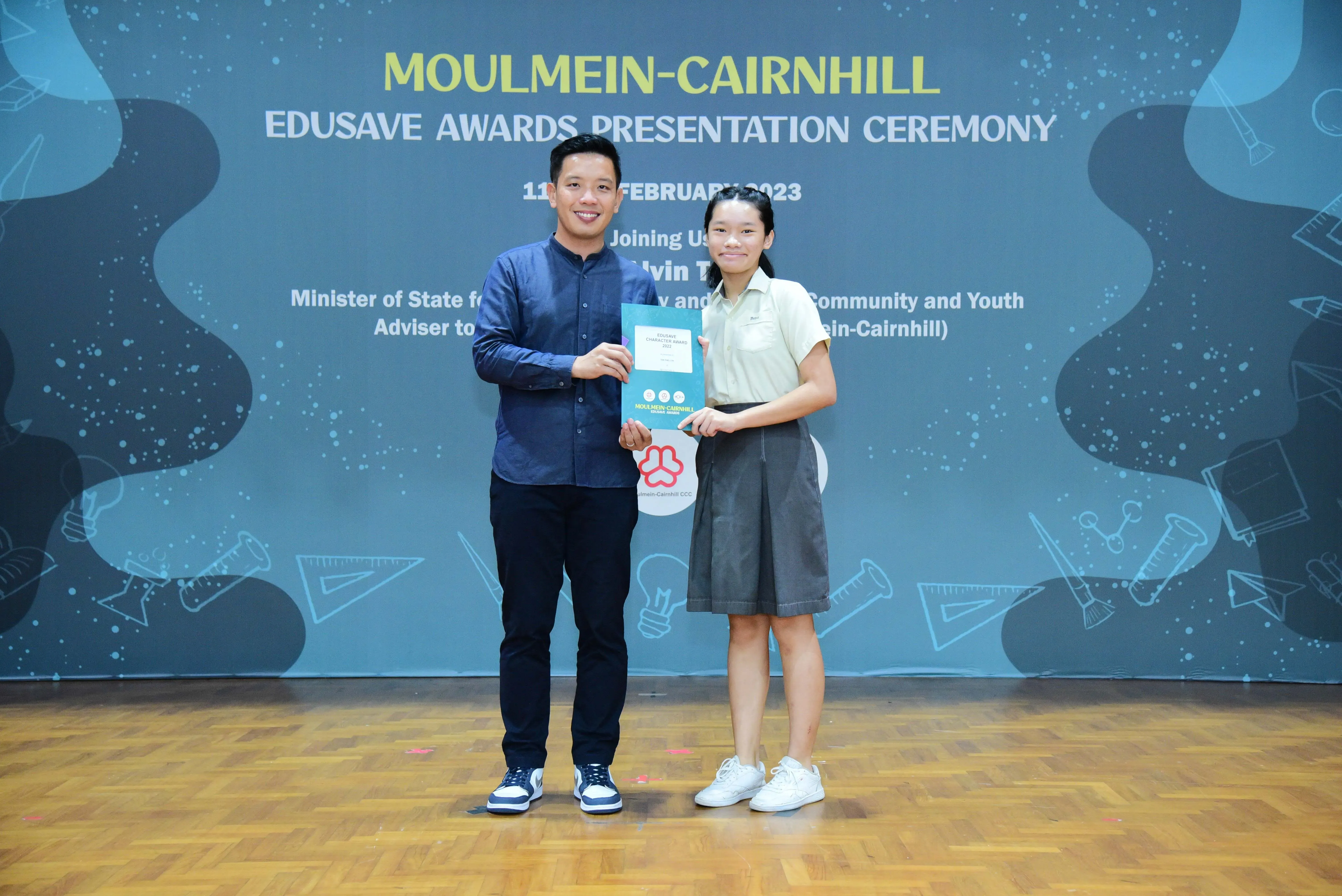 A man and a young girl hold a certificate together at the Moulmein-Cairnhill Edusave Awards Presentation Ceremony 2023.