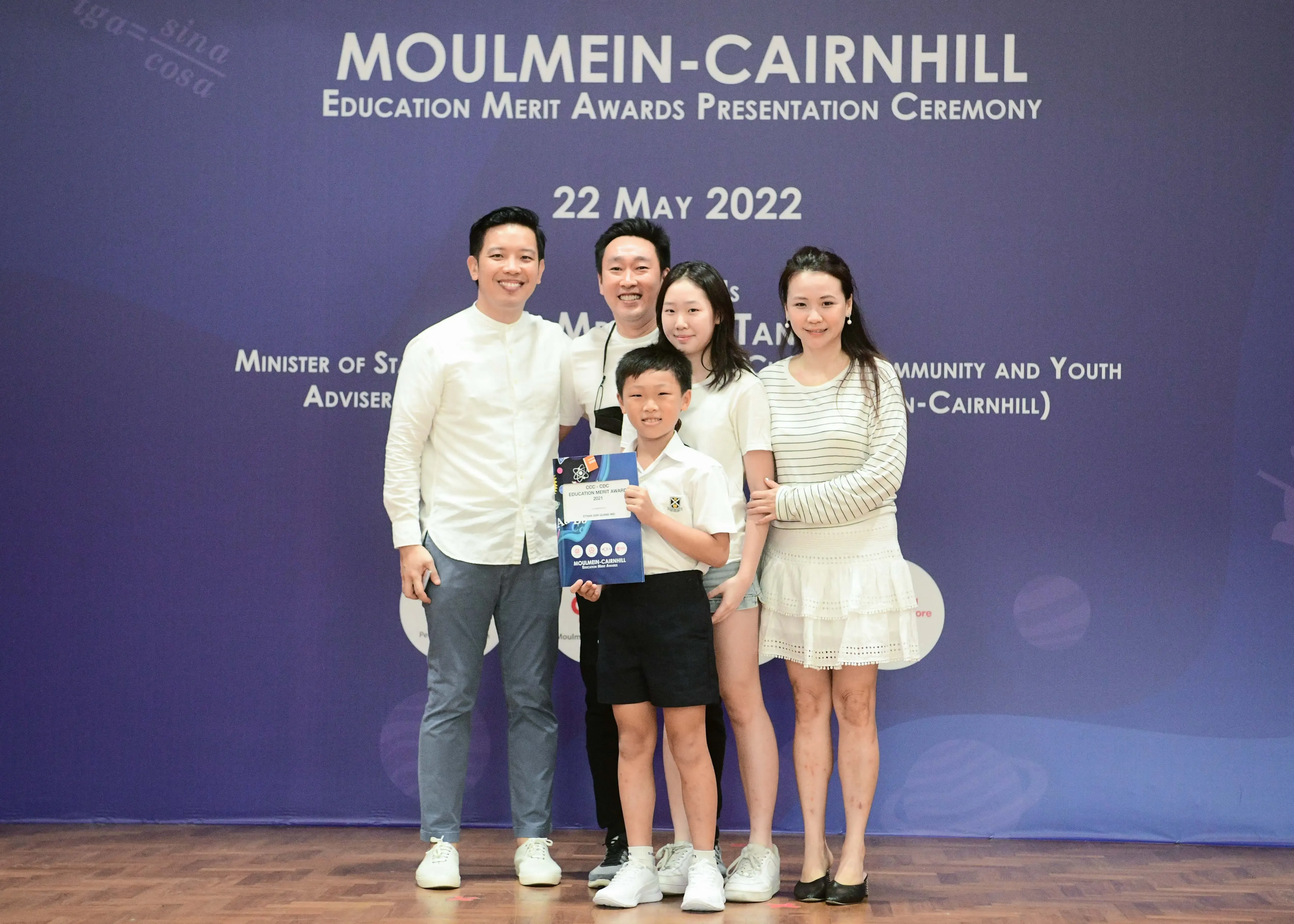 Four adults and a boy holding a certificate pose at the Moulmein-Cairnhill Education Merit Awards on 22 May 2022.