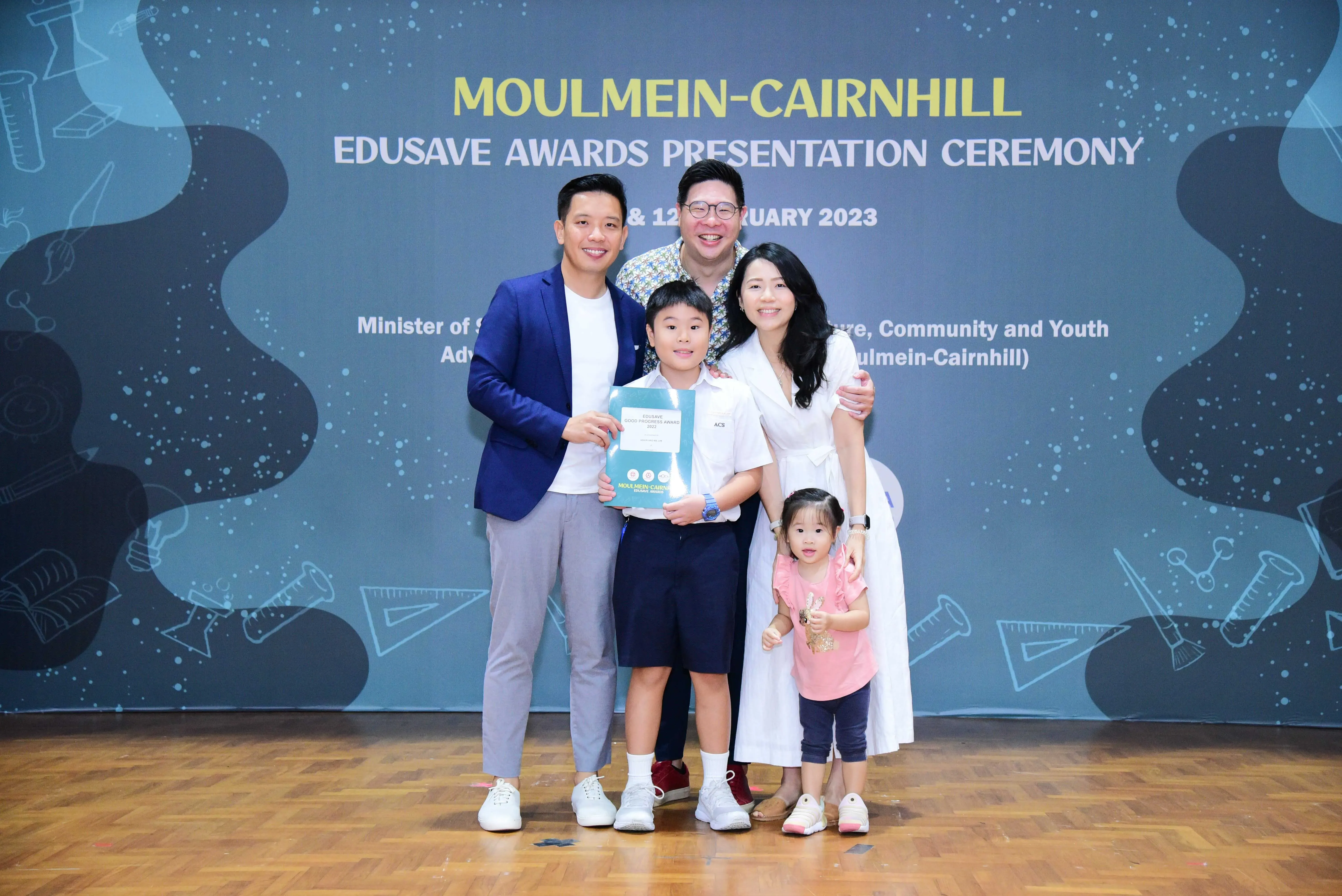 A family of five poses with an award certificate at the Moulmein-Cairnhill Edusave Awards Presentation Ceremony 2023.