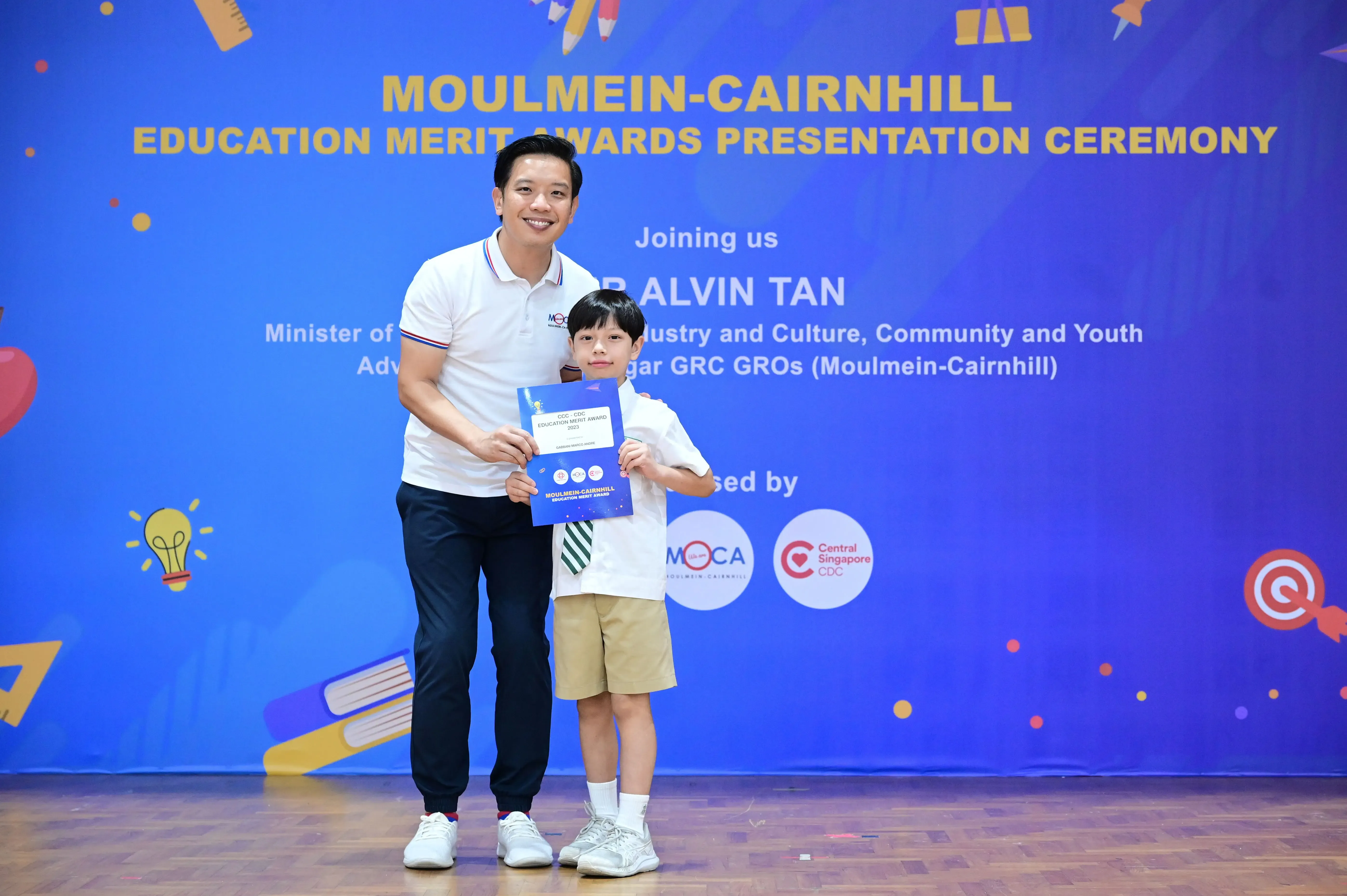 A man and a young boy hold a certificate at the Moulmein-Cairnhill Education Merit Awards Presentation Ceremony.
