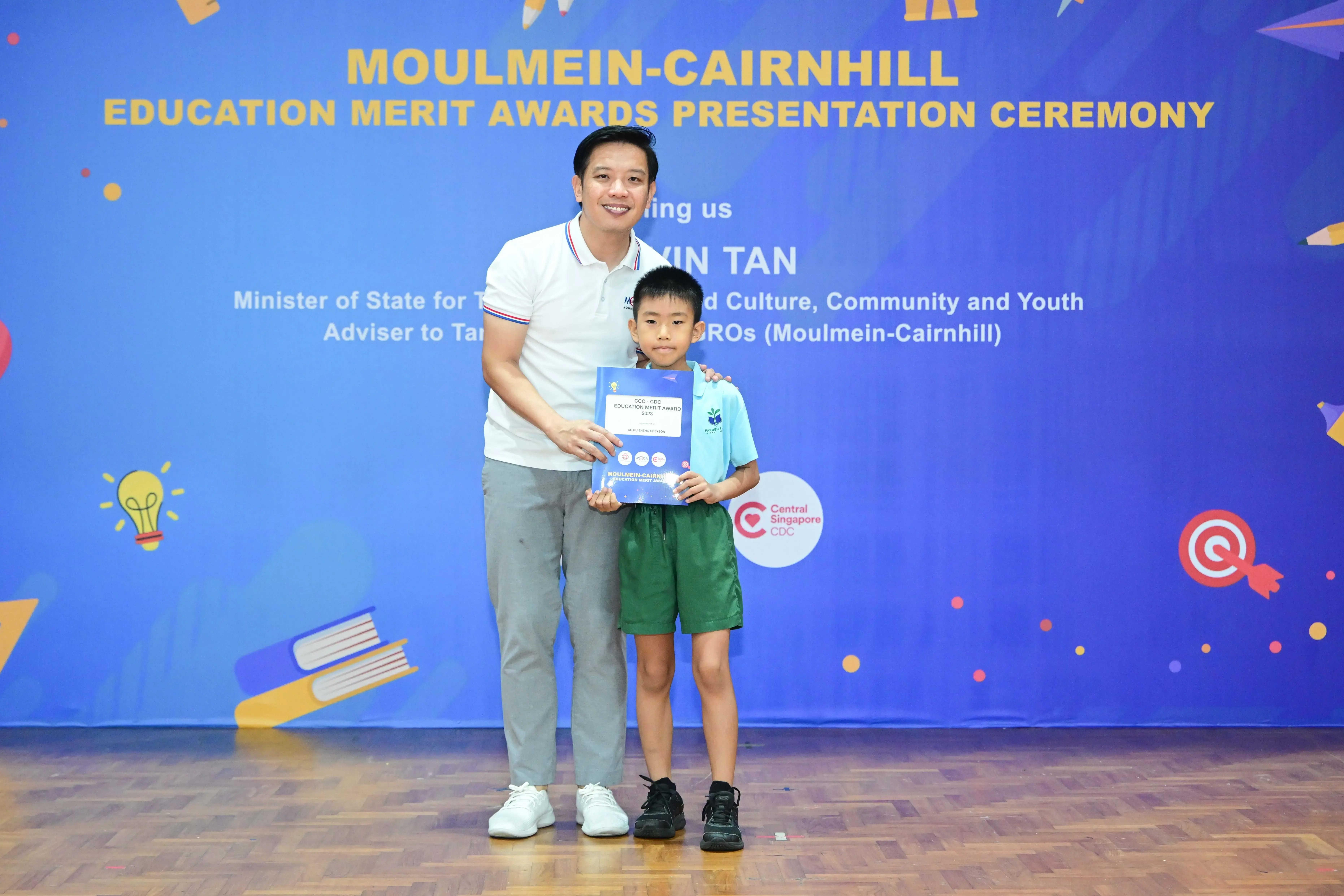 A man and a young boy hold a certificate at the Moulmein-Cairnhill Education Merit Awards Presentation Ceremony.
