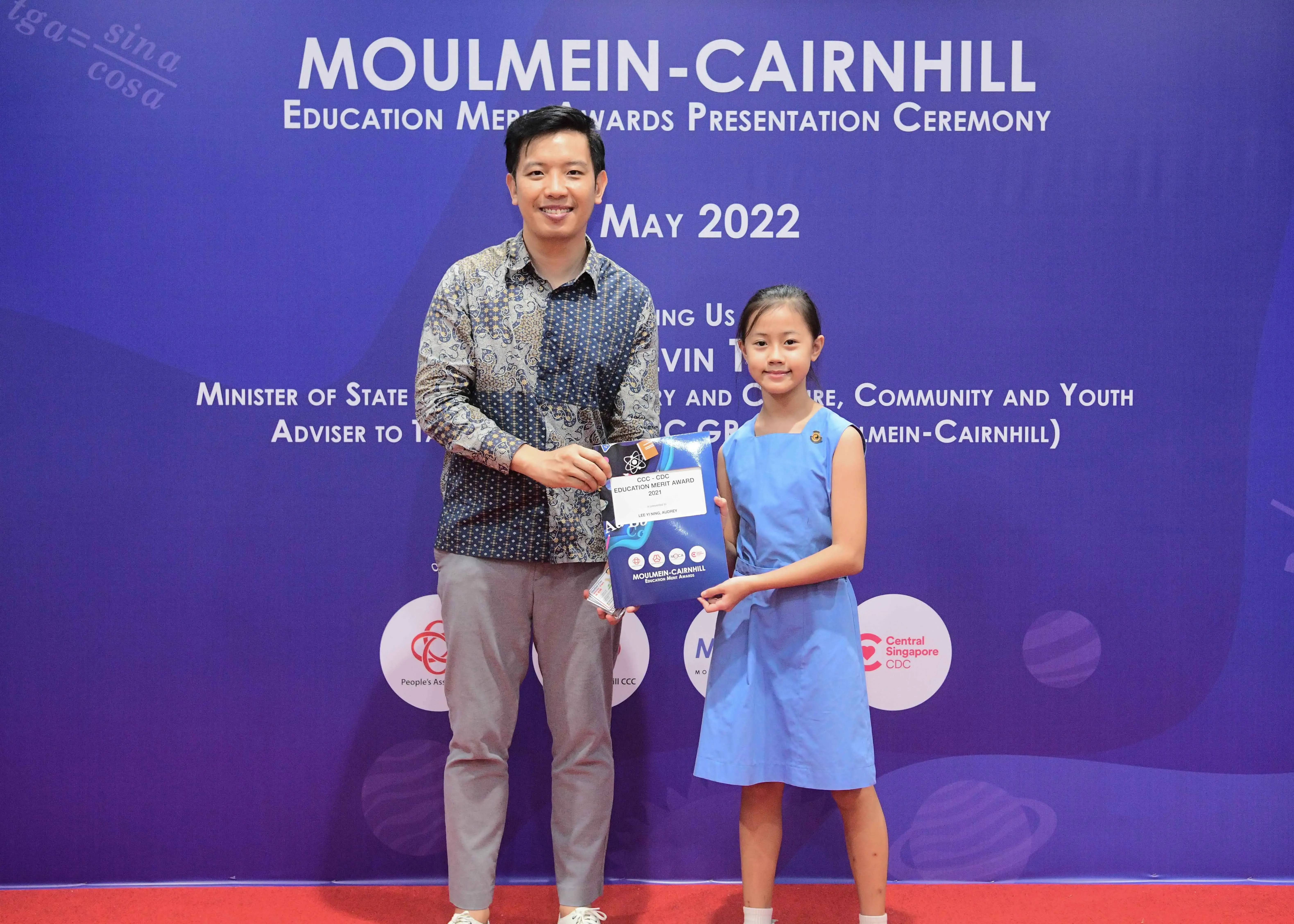 A man and a young girl hold an award certificate at the Moulmein-Cairnhill Education Merit Awards Ceremony, May 2022.