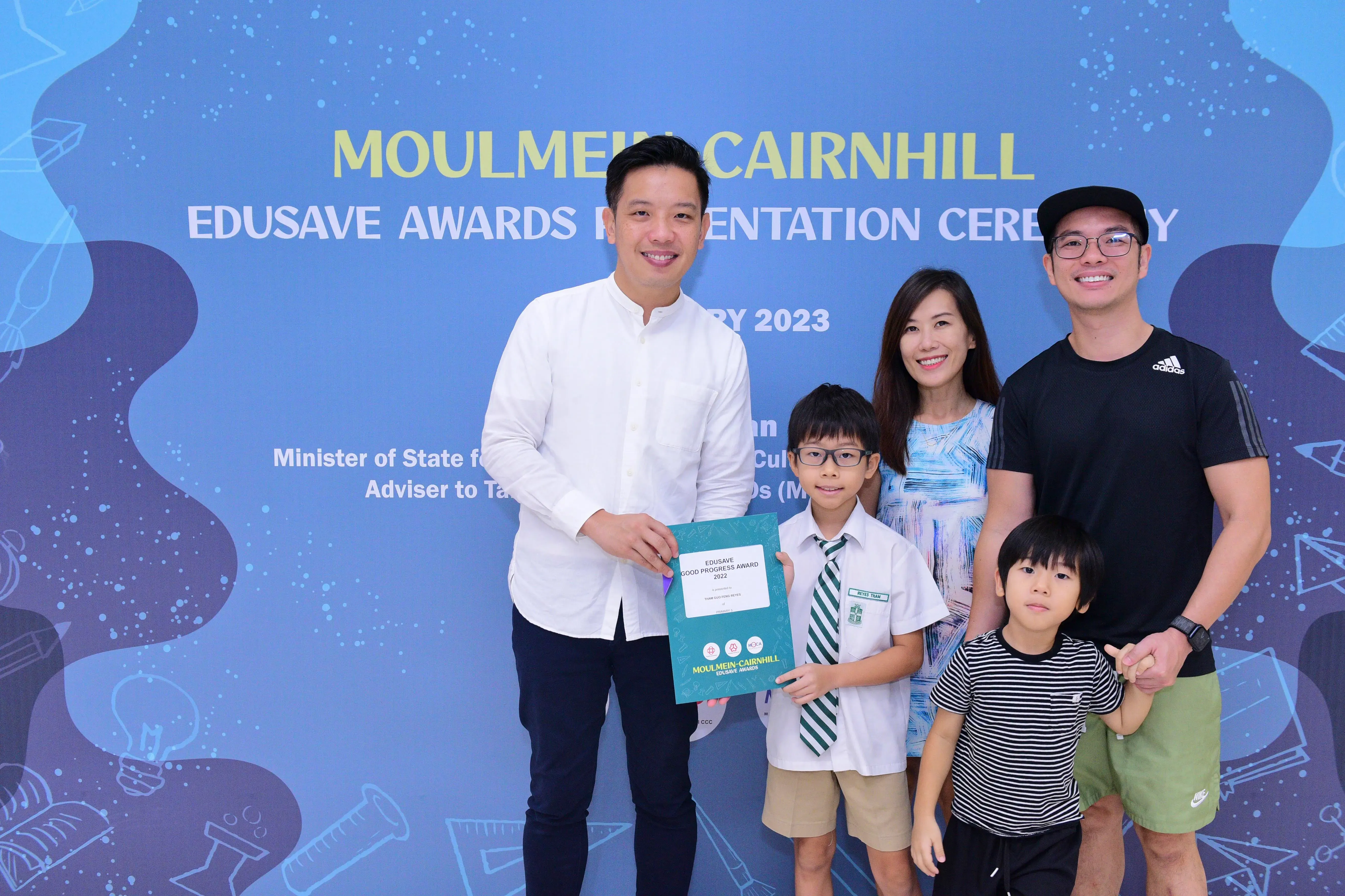 A boy holds an Edusave Good Progress Award certificate with three adults and a younger child at the 2023 ceremony.