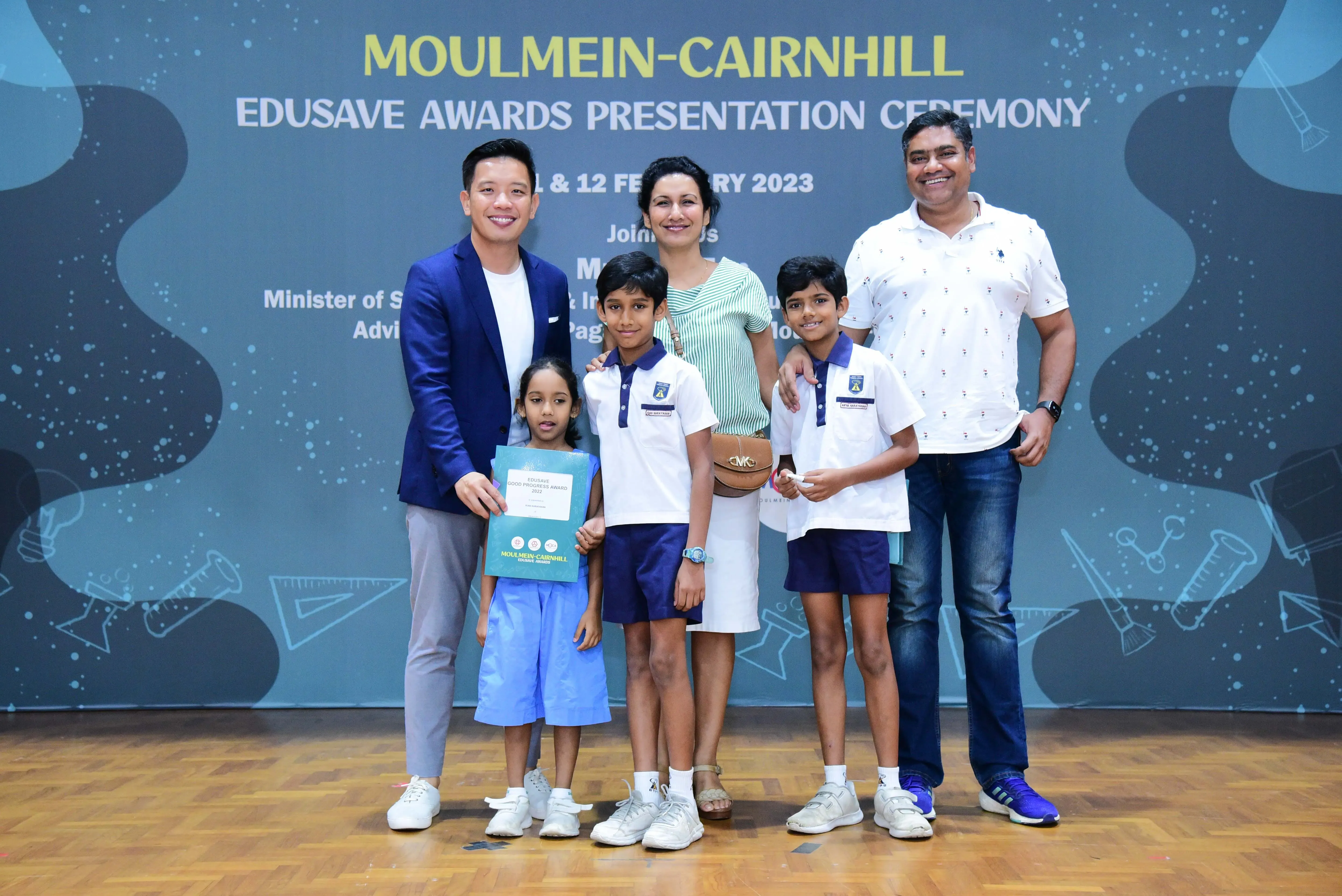 Five people pose at the Moulmein-Cairnhill Edusave Awards Presentation Ceremony 2023, including three children holding certificates.