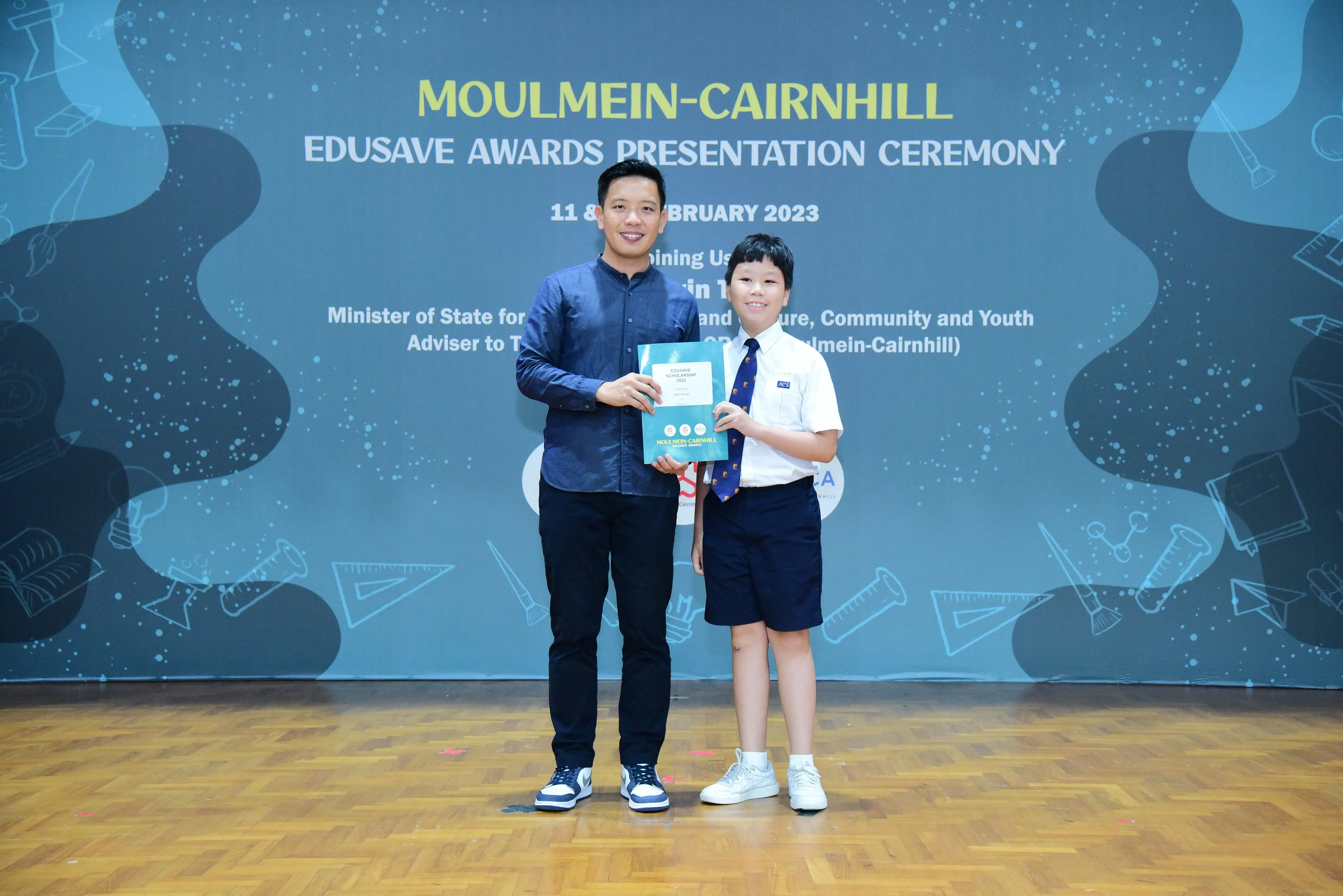 An adult and a uniformed student hold a certificate at the Moulmein-Cairnhill Edusave Awards Ceremony 2023.