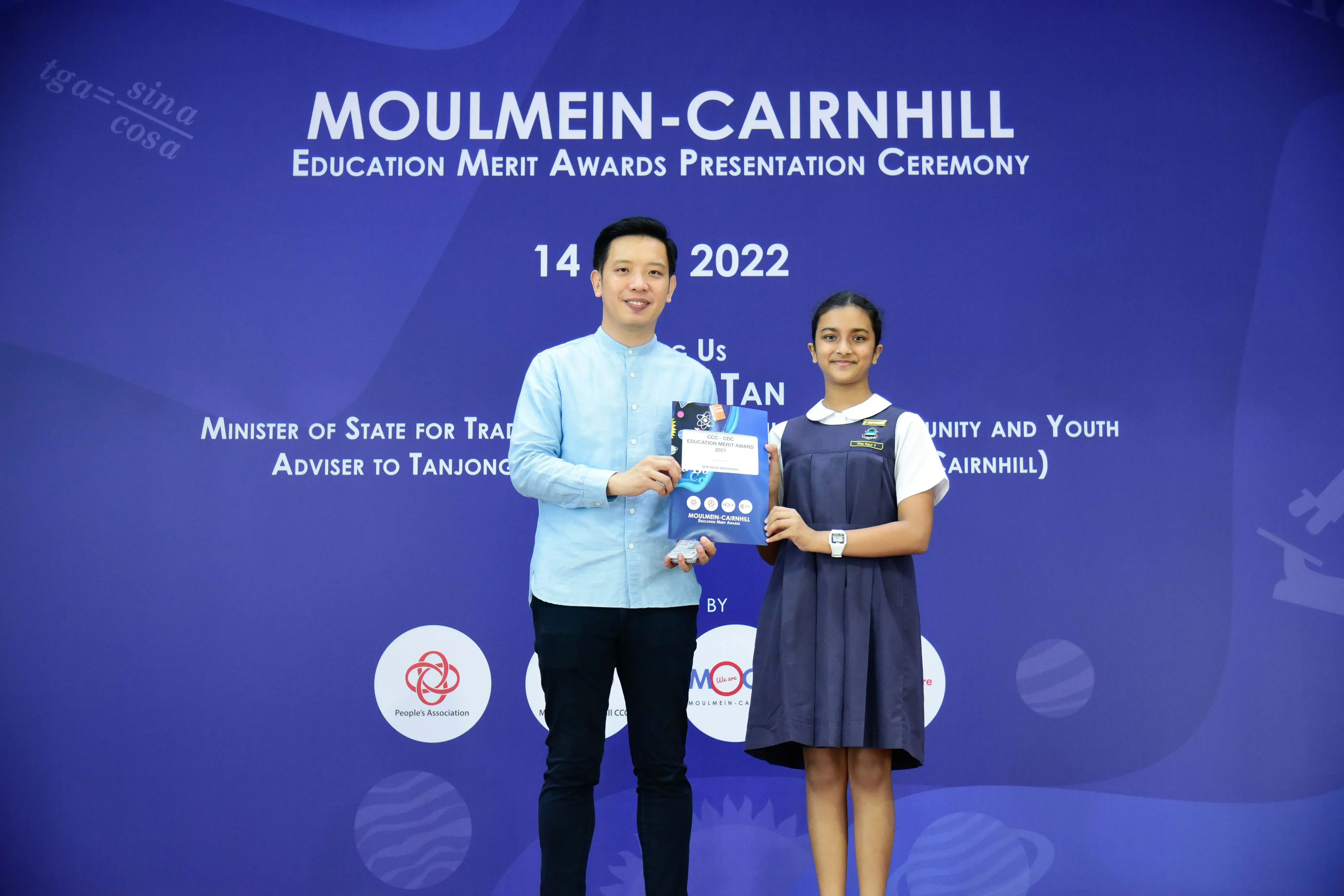 A man and a young girl in school uniform hold an award certificate at the 2022 Moulmein-Cairnhill Education Merit Awards ceremony.