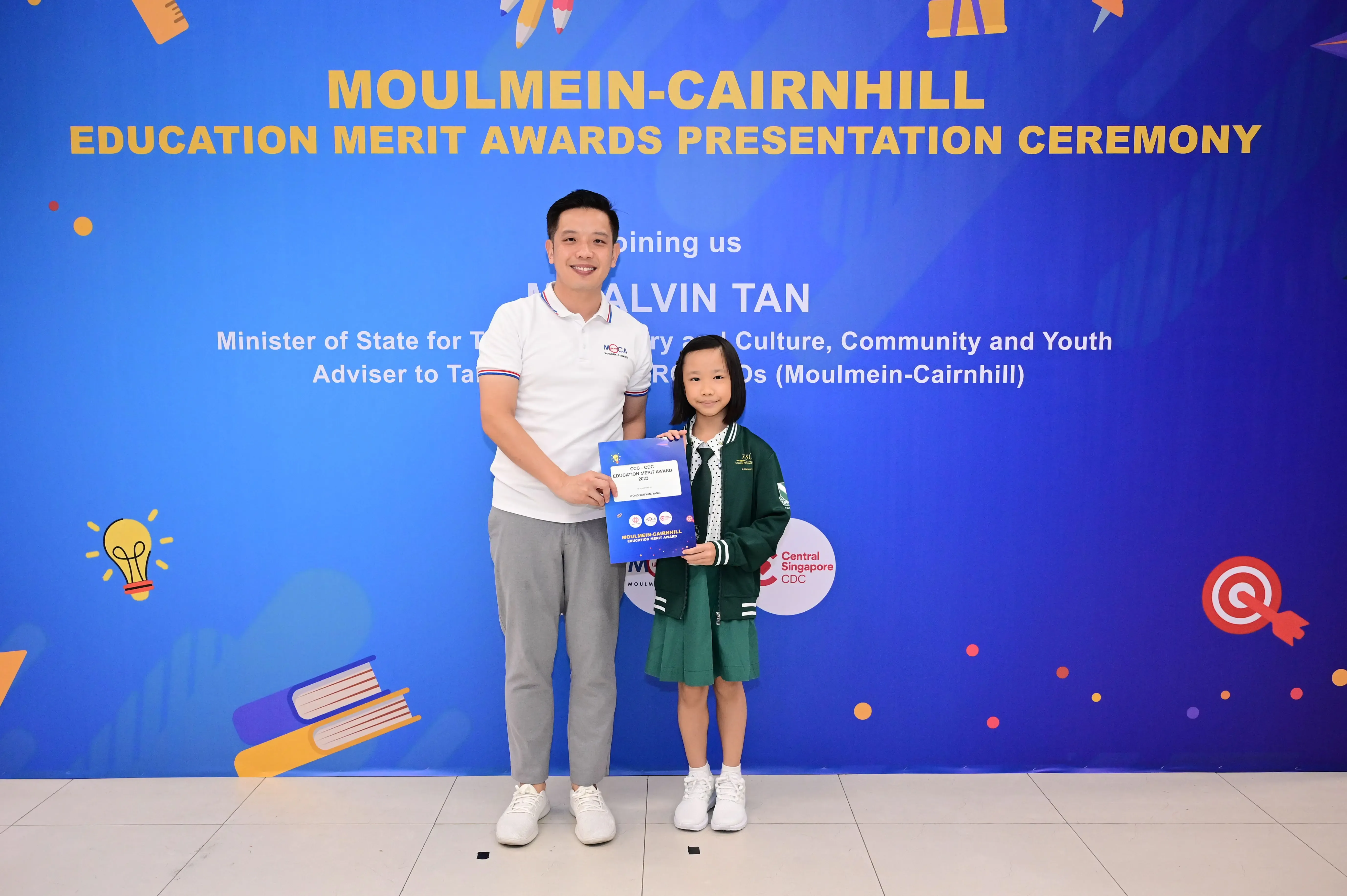 A man and a young girl hold a certificate at the Moulmein-Cairnhill Education Merit Awards Presentation Ceremony.