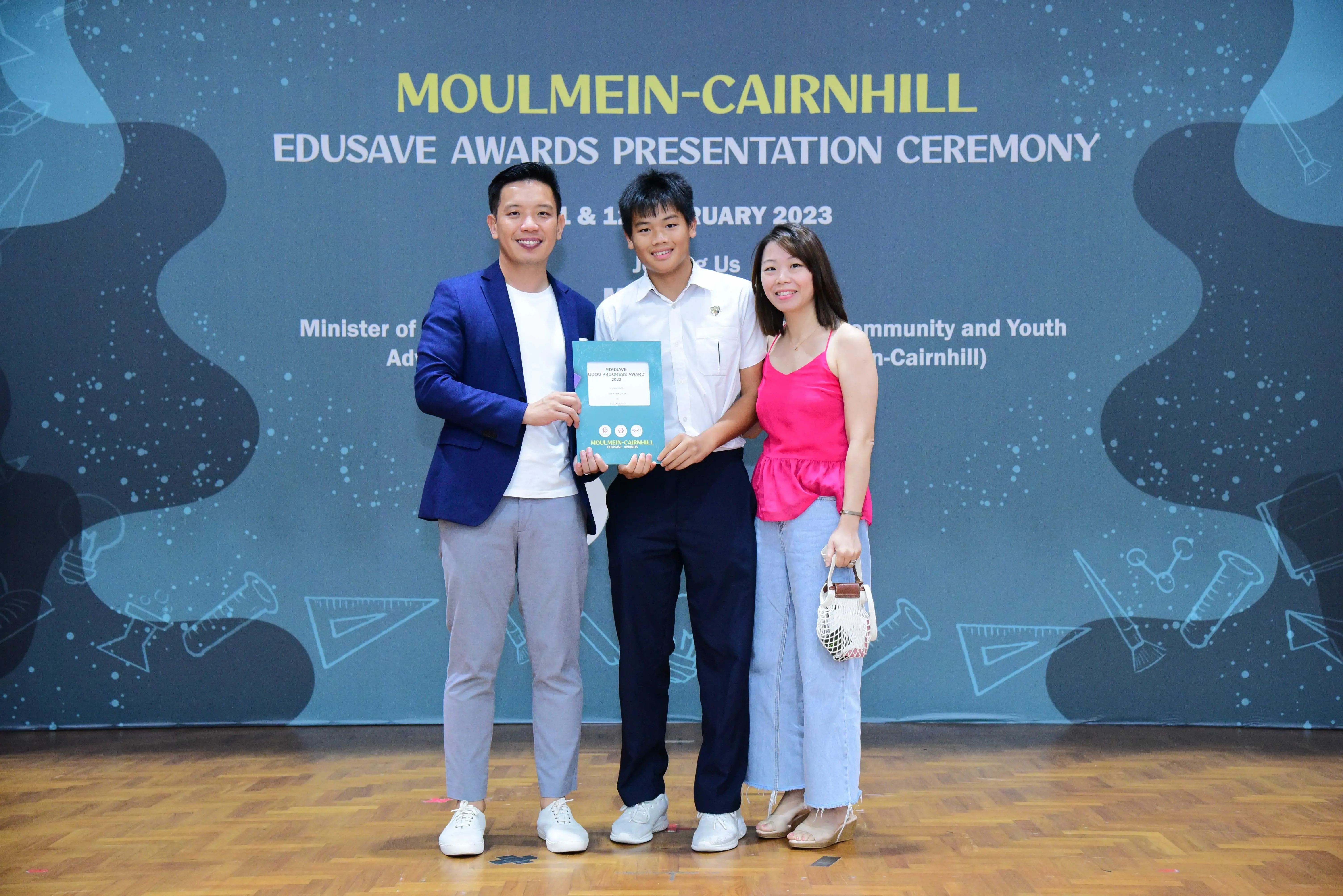 Three people smile holding an award at the Moulmein-Cairnhill Edusave Awards Presentation Ceremony 2023.
