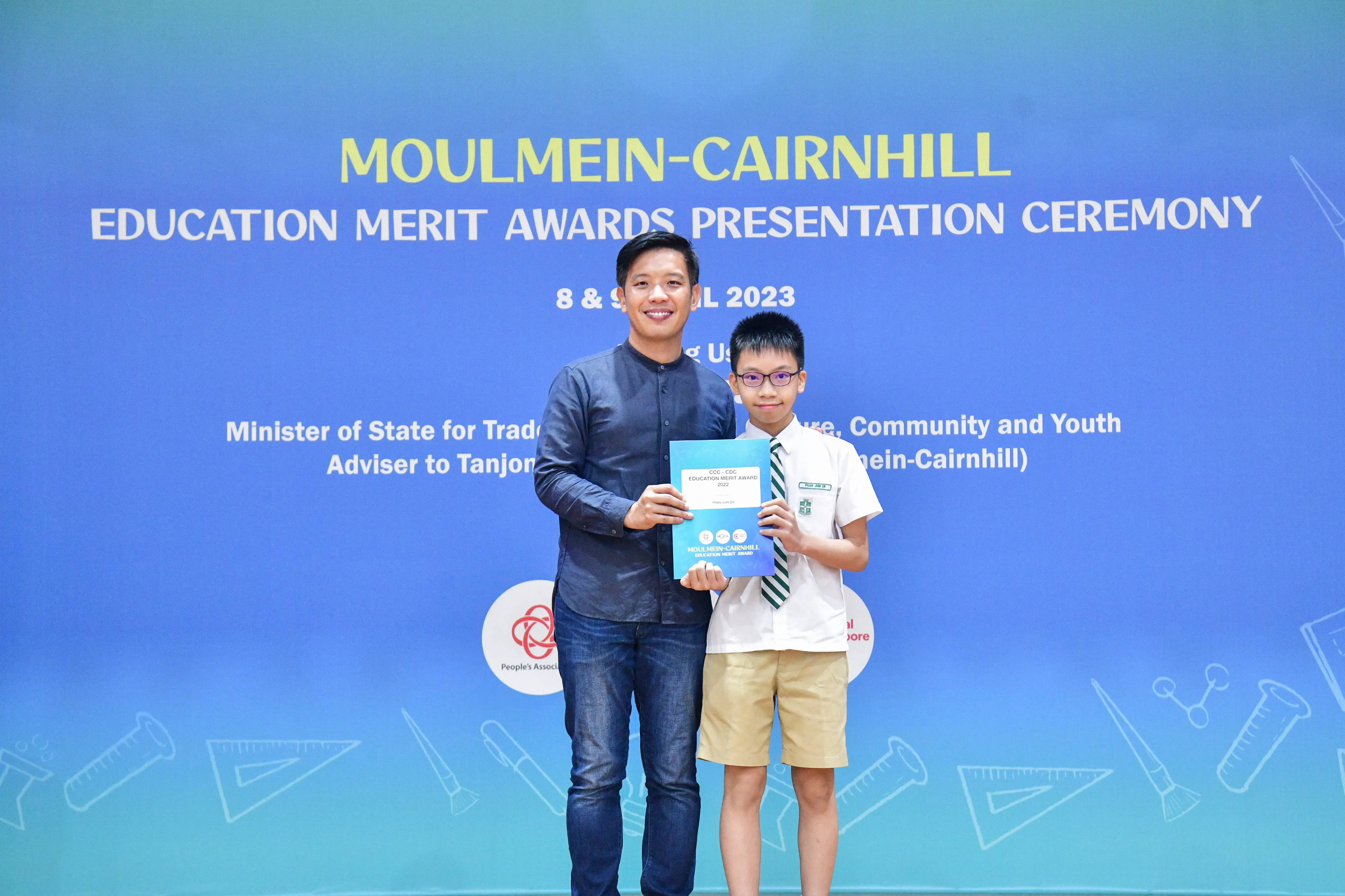 A man and a young boy in school uniform hold an award certificate at the Moulmein-Cairnhill Education Merit Awards 2023.