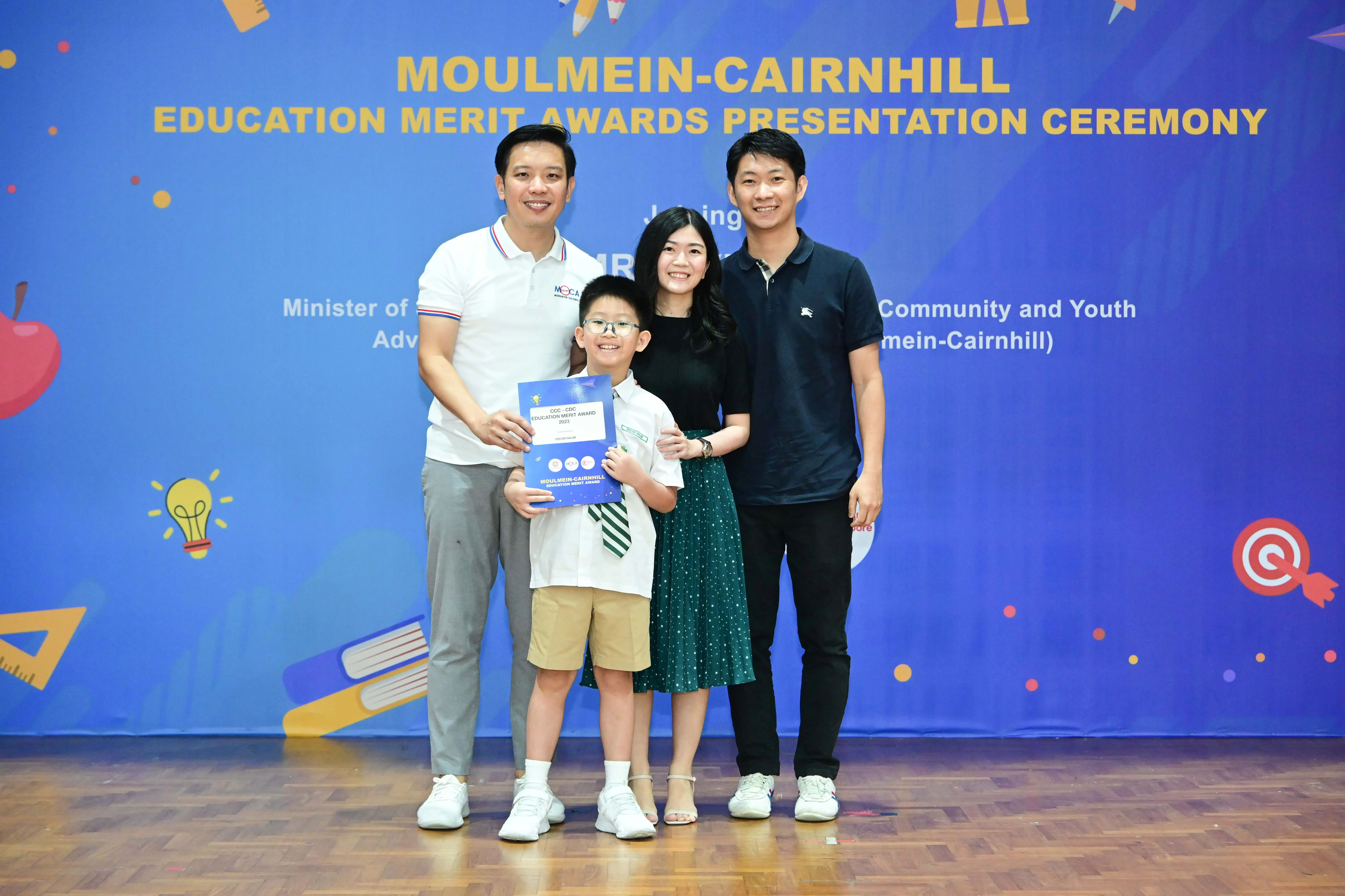 Three adults and a boy holding a certificate pose at the Moulmein-Cairnhill Education Merit Awards Ceremony.