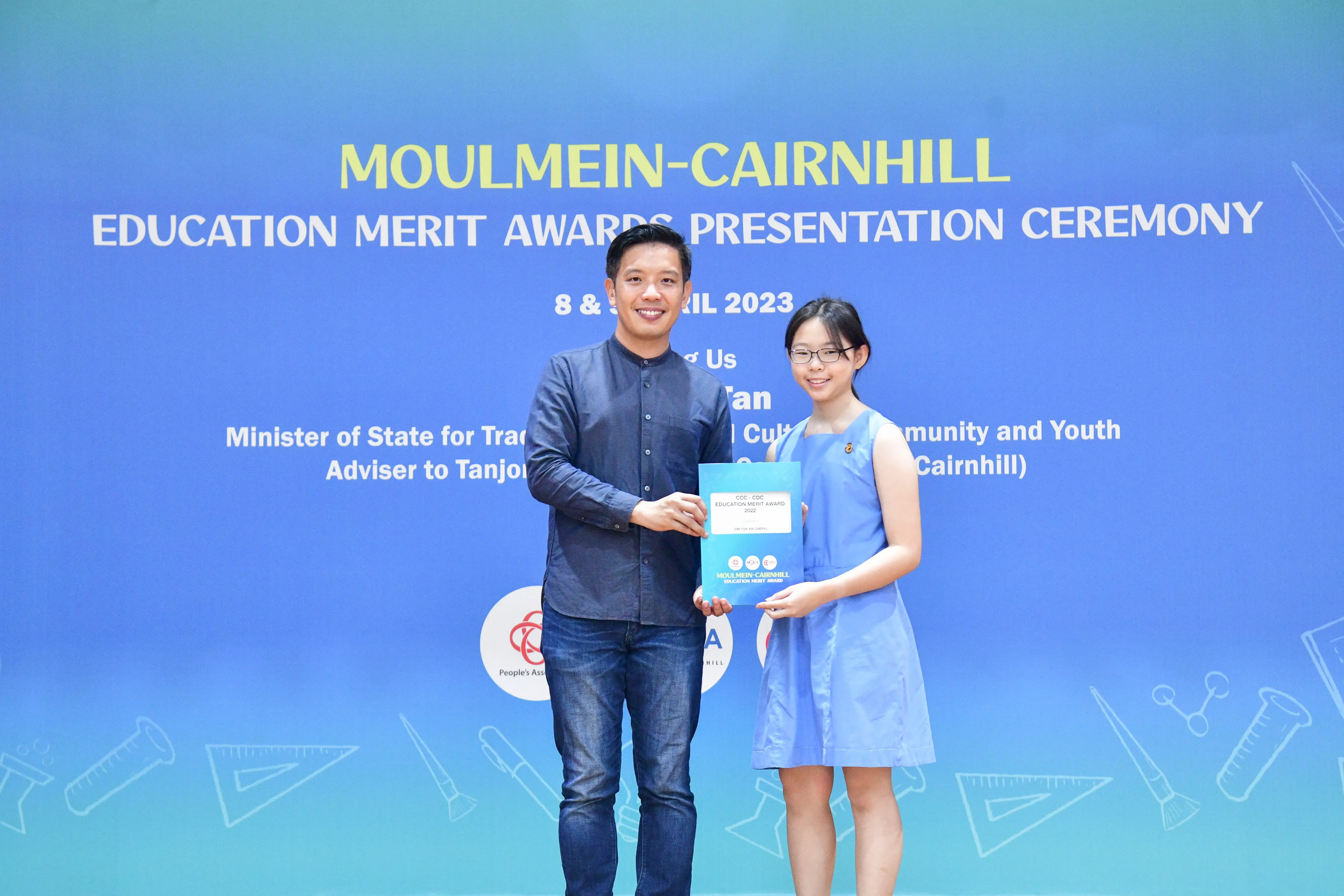 A man and a young girl hold a certificate together at the Moulmein-Cairnhill Education Merit Awards Ceremony, April 2023.