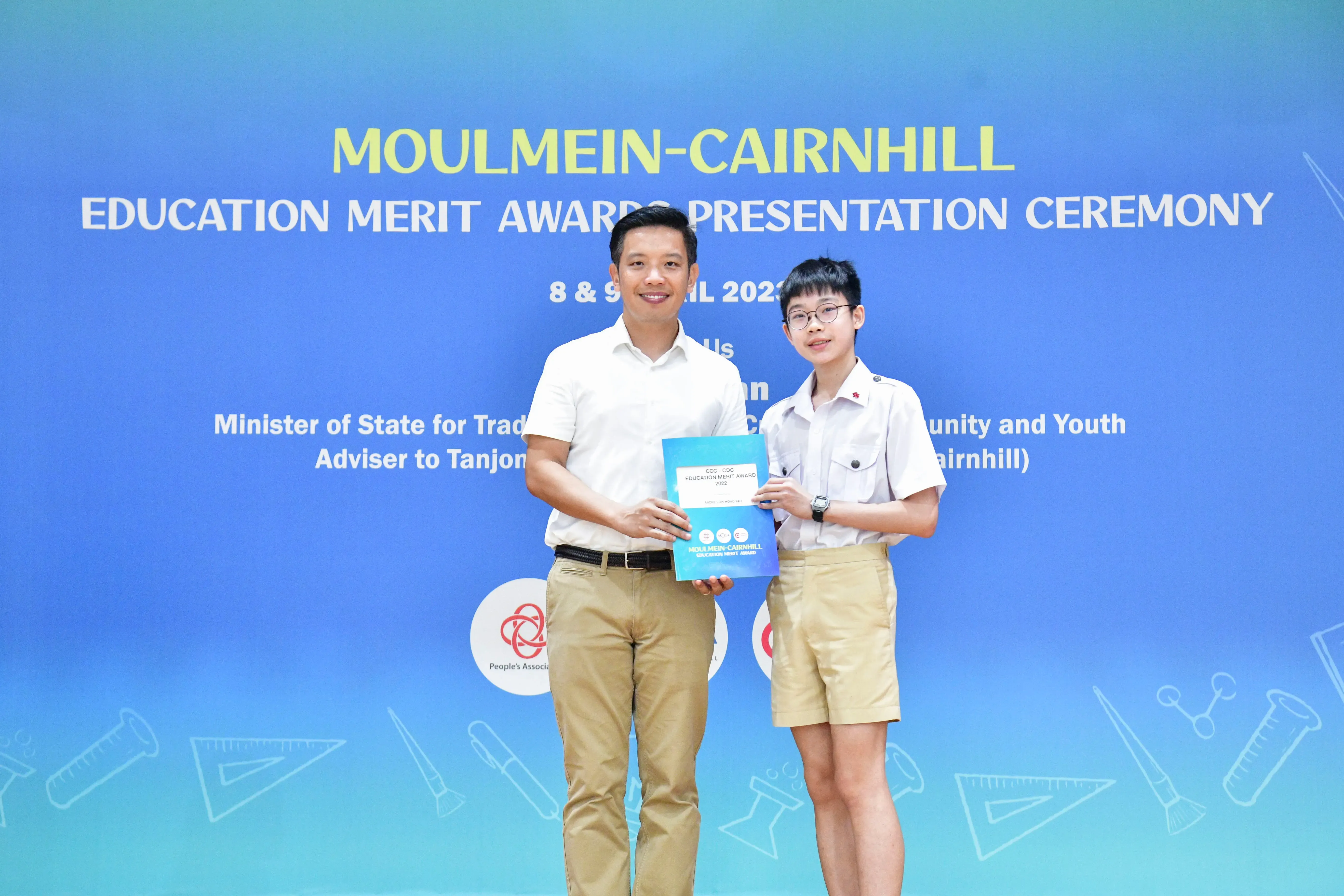 An adult and a young student hold an award booklet at the Moulmein-Cairnhill Education Merit Awards Presentation Ceremony.