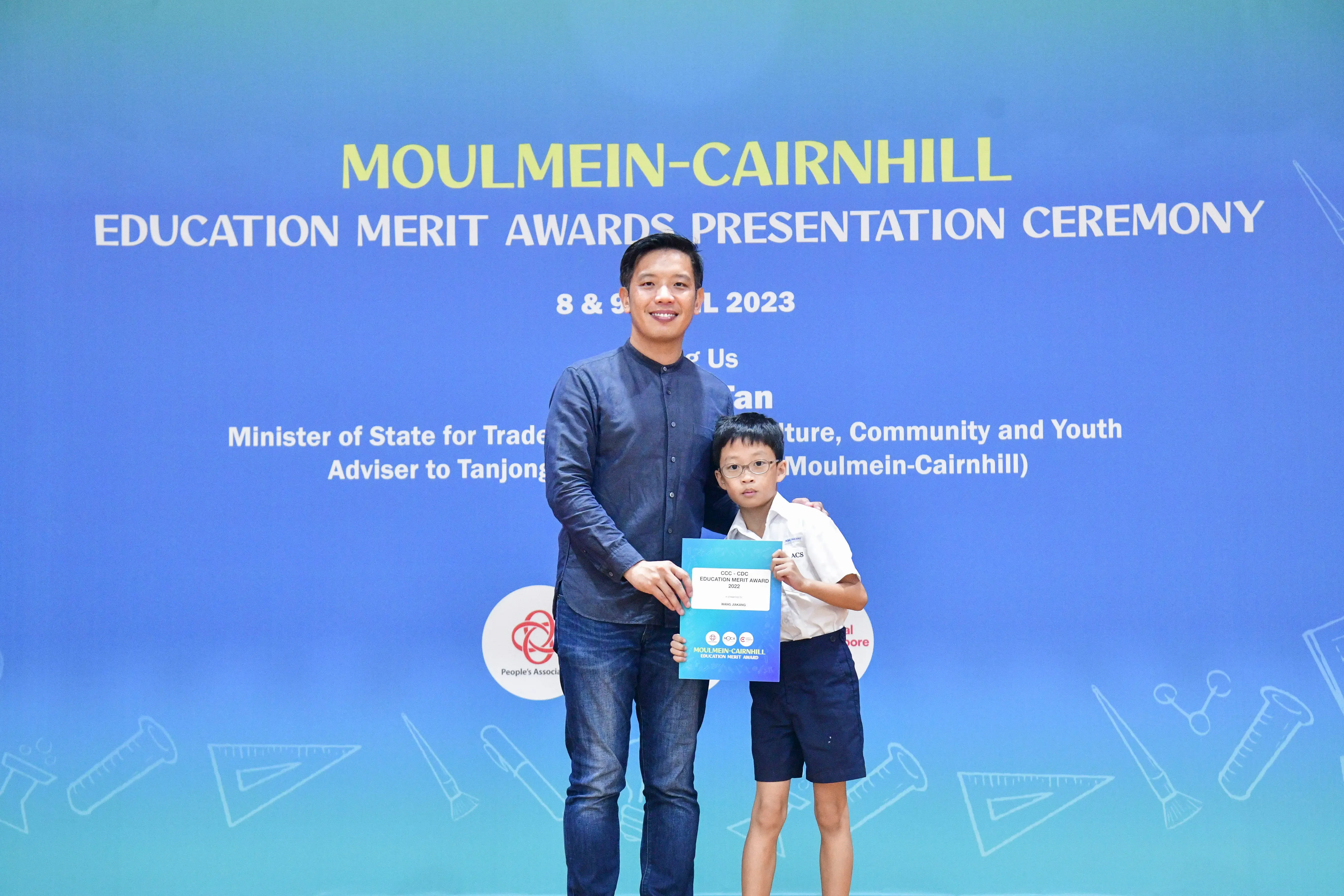 An adult and a young boy hold an award certificate at the Moulmein-Cairnhill Education Merit Awards Ceremony 2023.